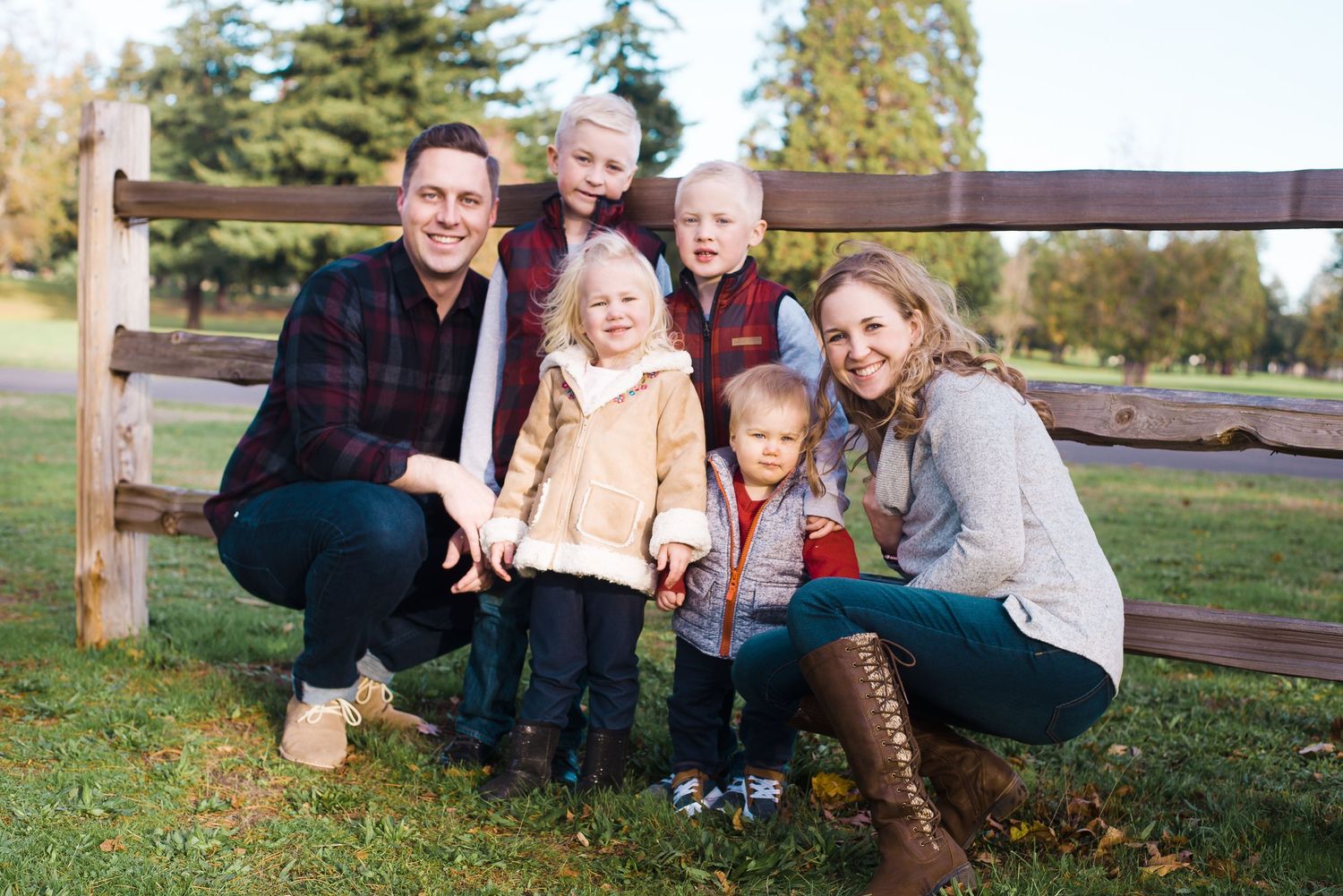 Natural light family portrait captured beside a rustic wooden fence during golden hour.