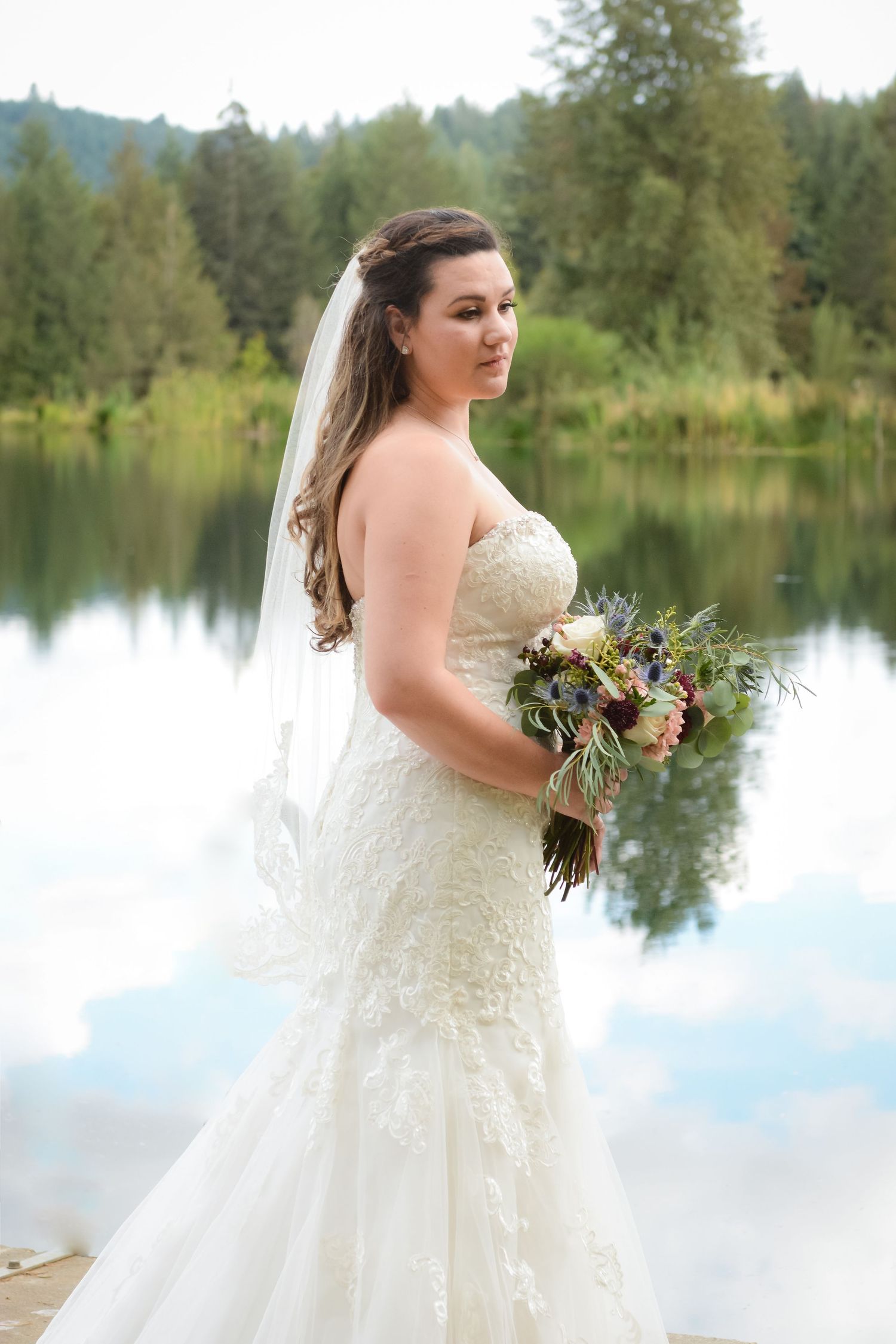 Bride holding her bouquet beside a peaceful lake during a natural light wedding portrait session.