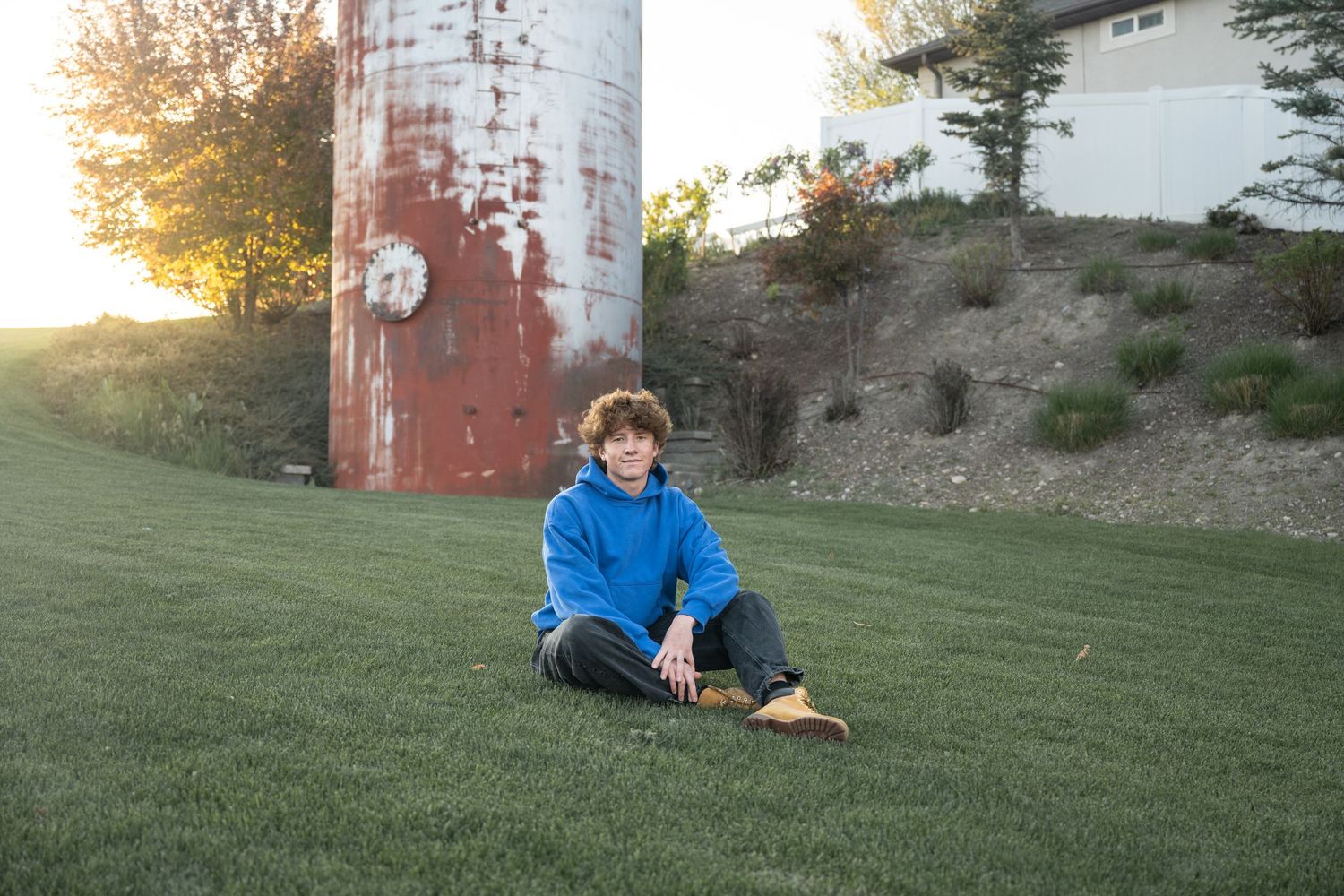 Young boy sitting on green grass near a rustic silo during an outdoor senior portrait session in Utah.