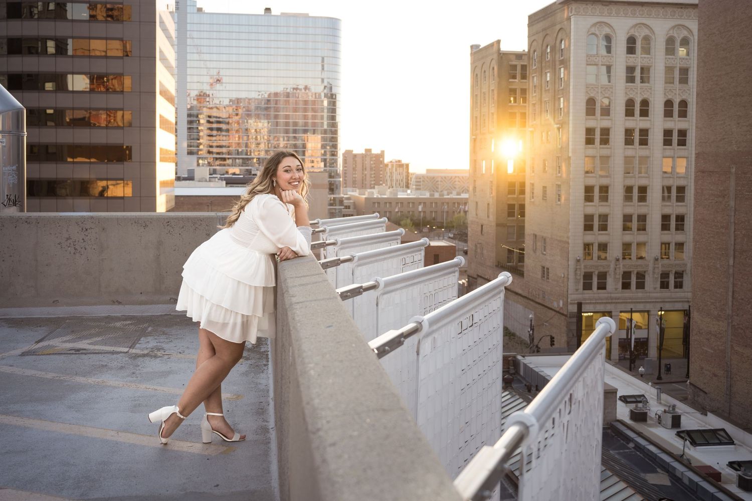 High school senior girl overlooking a downtown city skyline from a rooftop during a golden hour urban senior photography session.