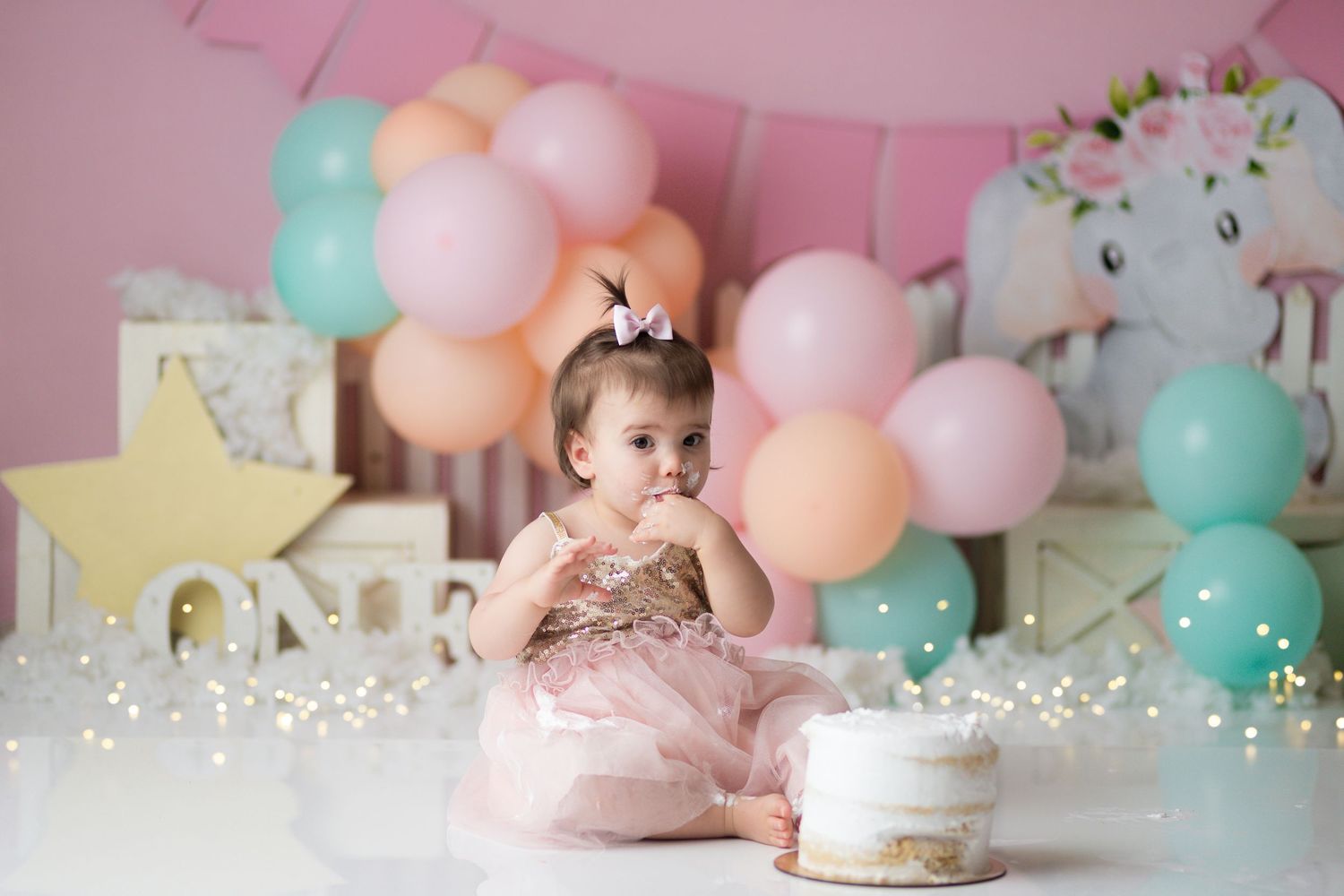 Pastel pink and mint balloon garland decorates a first birthday party with cake smash setup and floral accents.