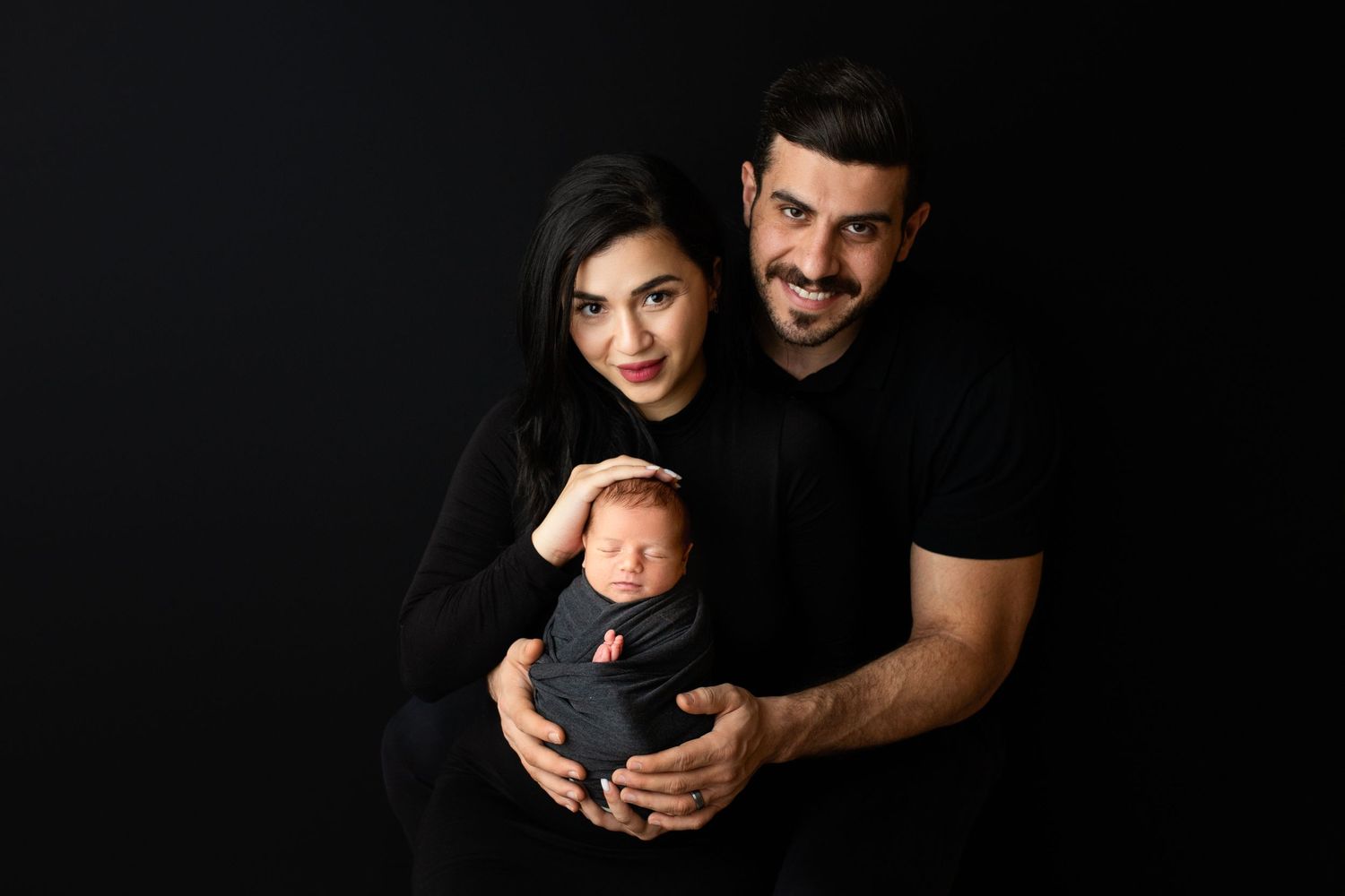 Studio portrait against black background showing intimate family moment.