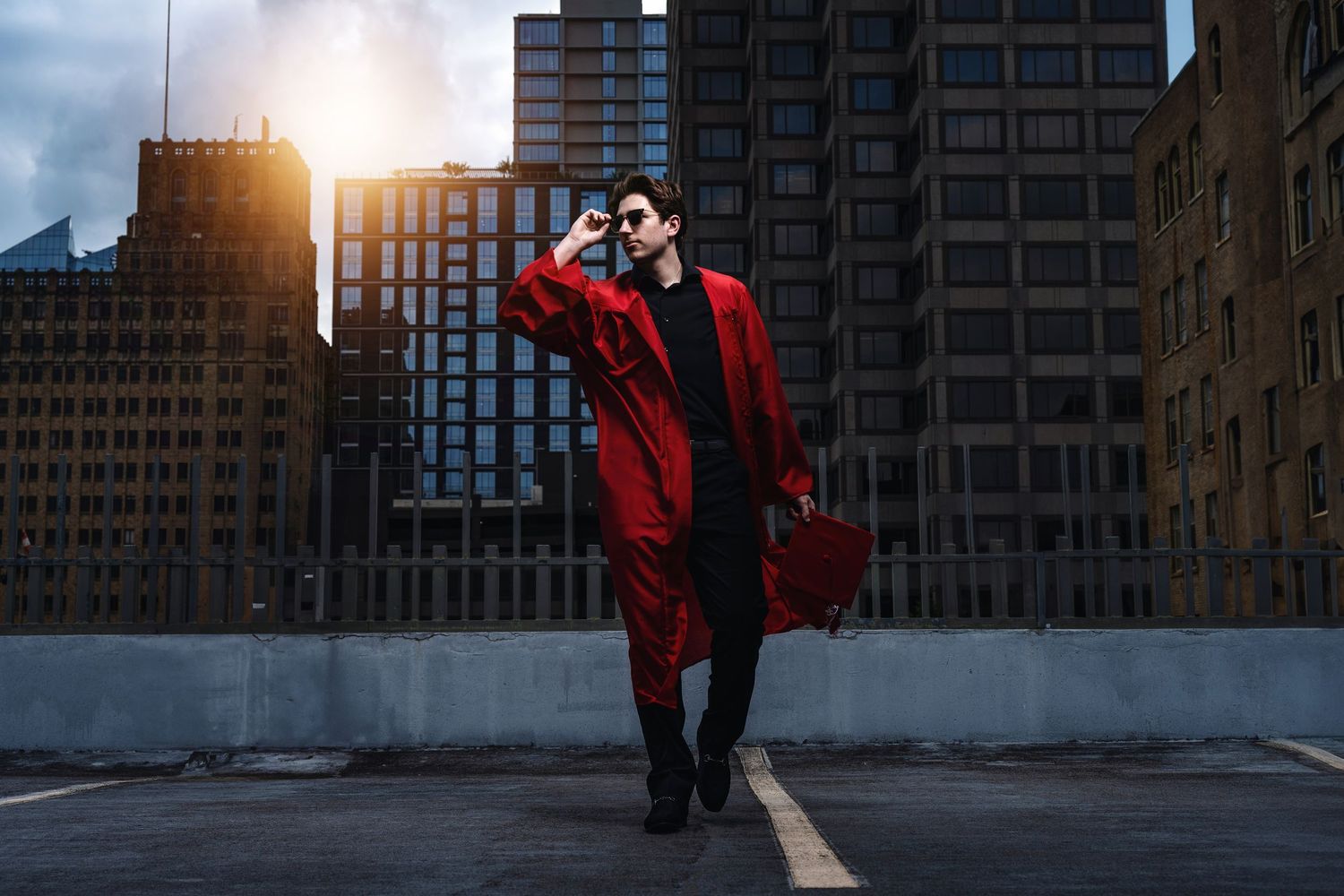 Person in red winter coat walks through city street at sunset with tall buildings in background.