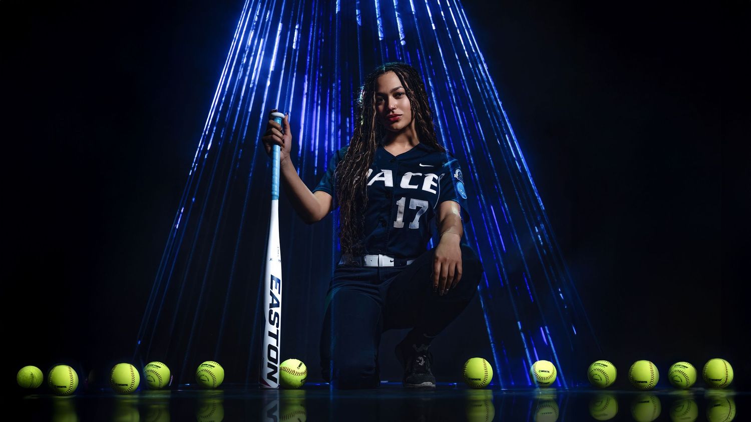 A tennis player poses with a racquet against a backdrop of blue lights with tennis balls lined up on the ground.