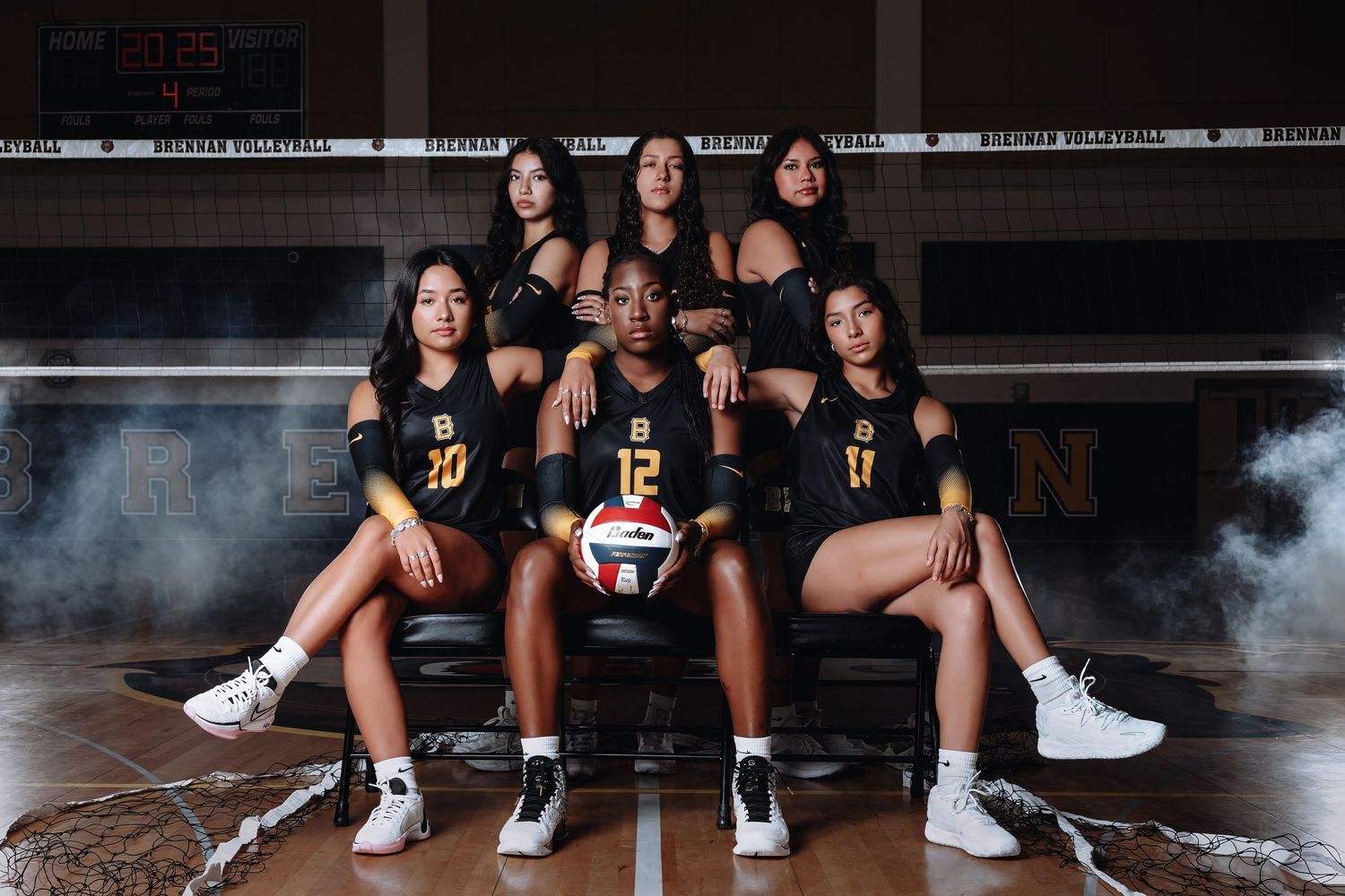 Indoor volleyball team poses for dramatic photo with smoke effects in black uniforms on wooden court.