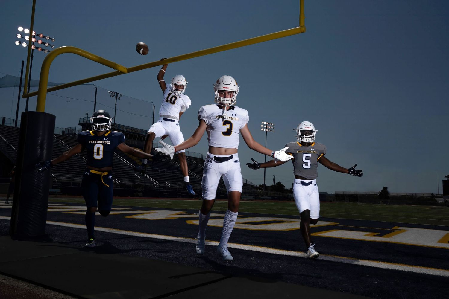 Football players pose in front of goal post in white uniforms during outdoor photo shoot.