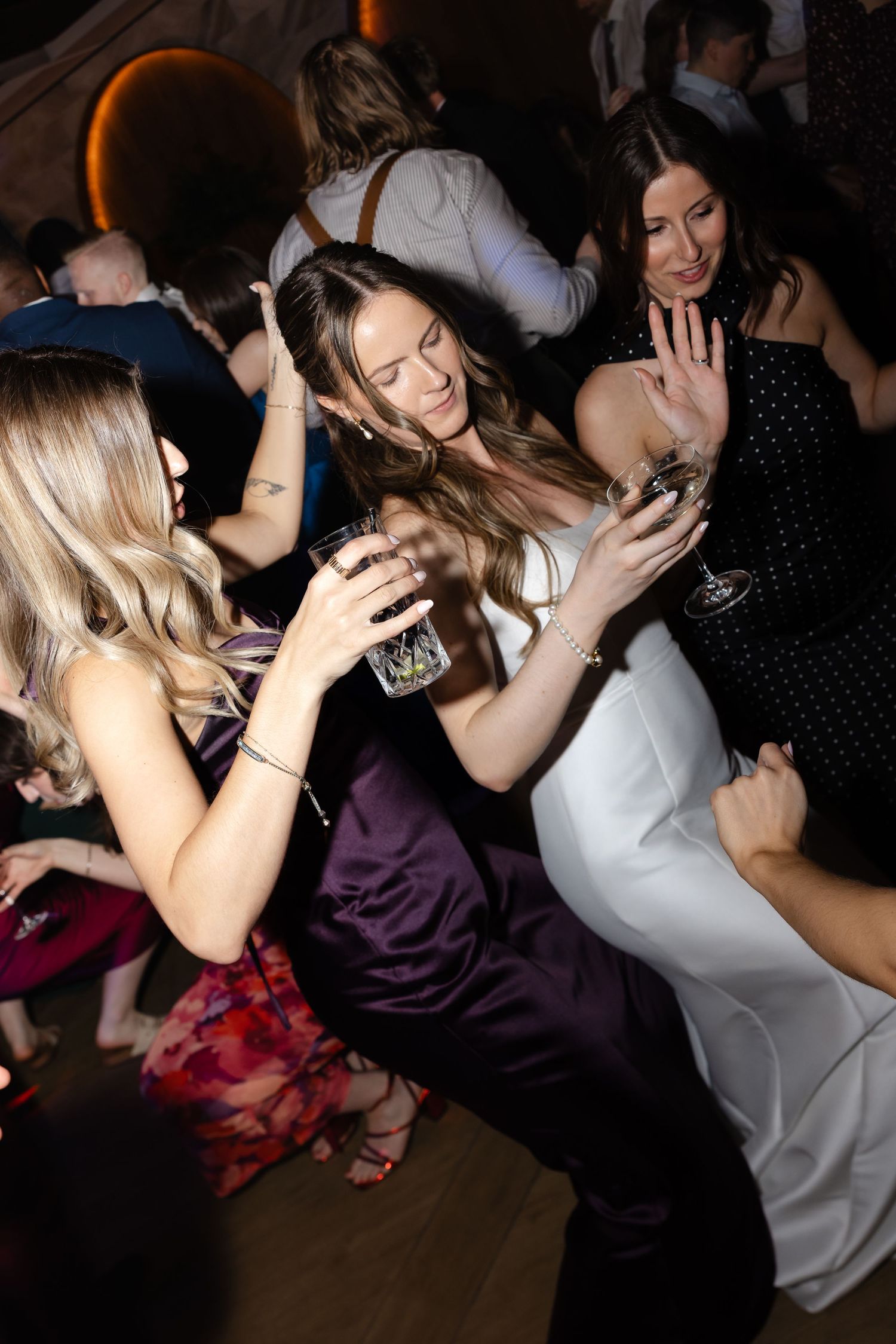 Women in elegant dresses dancing and socializing at a formal wedding reception party.