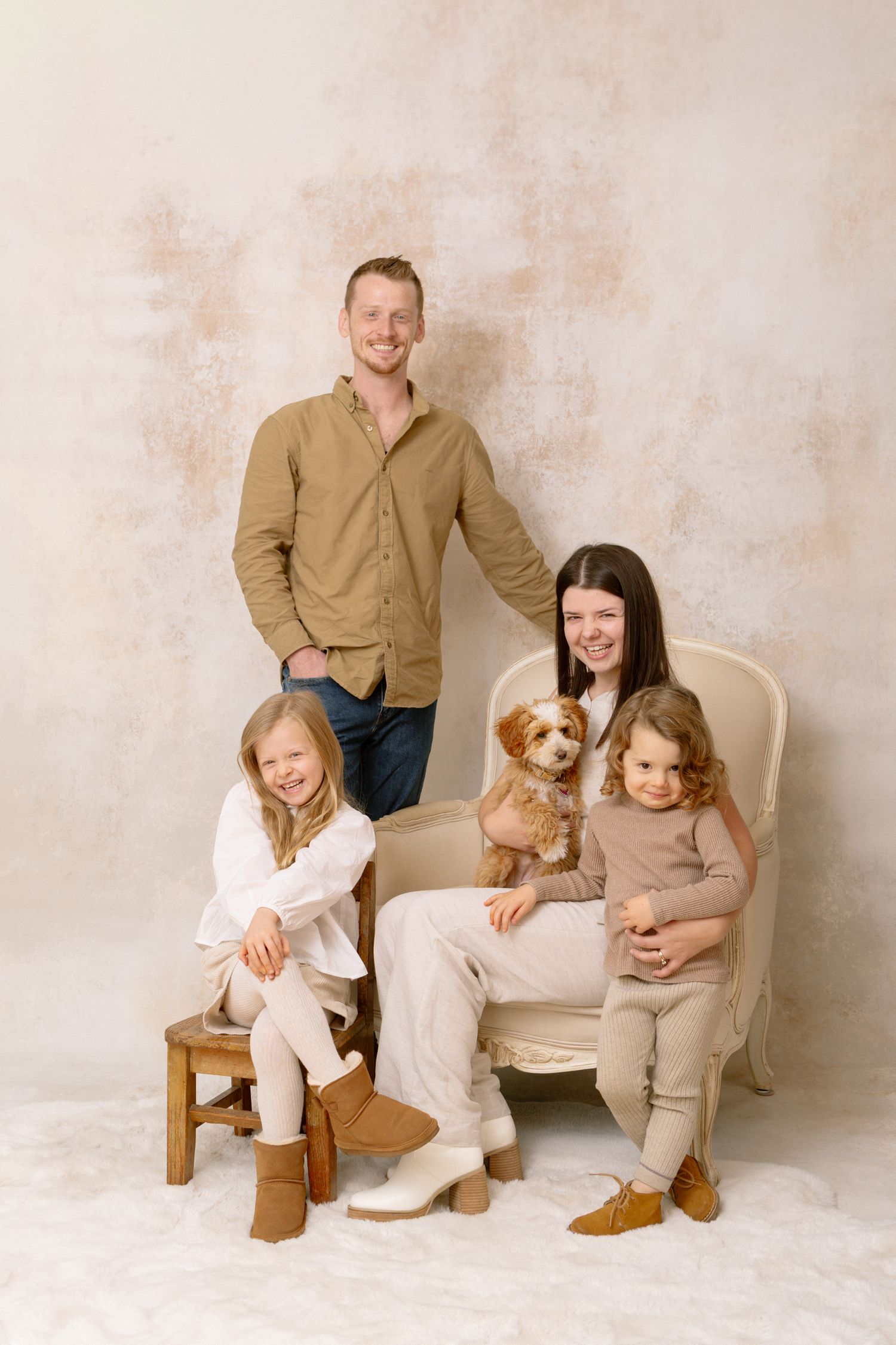Casual family photo session with pets on cream colored furniture against neutral background.