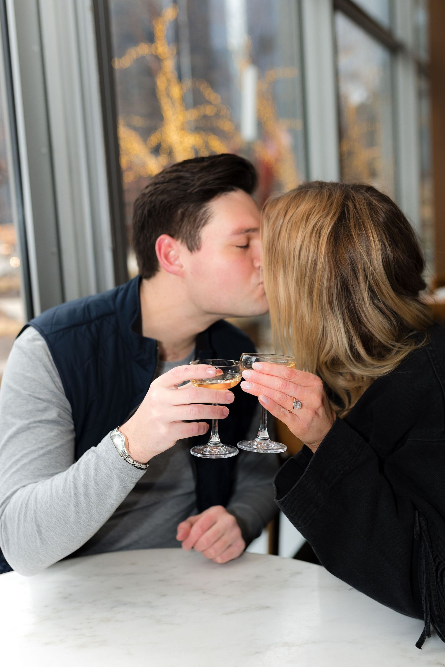 Couple sharing a romantic kiss while holding cocktail glasses at a restaurant table.