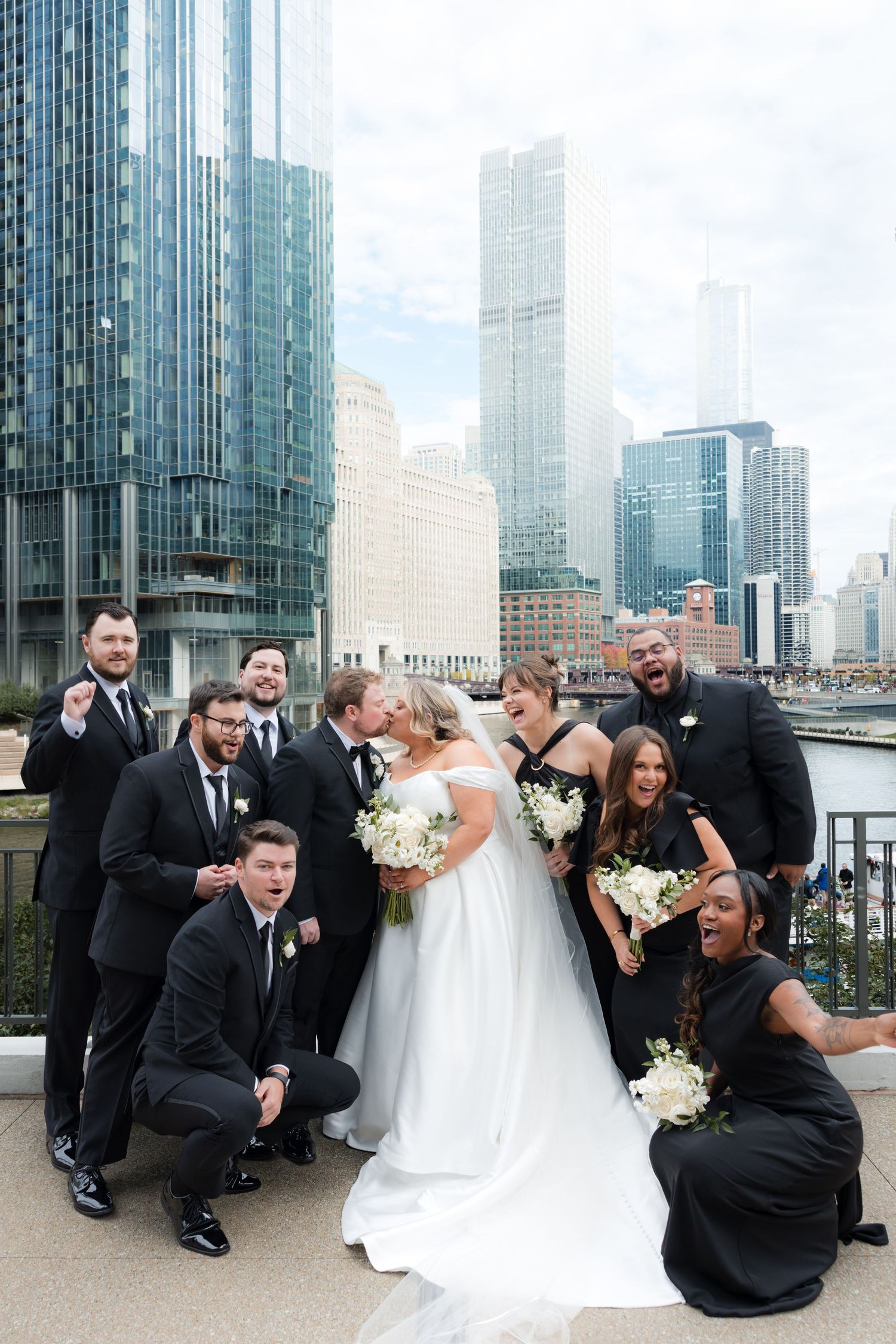 Wedding party having fun with candid group photos in front of modern glass buildings.