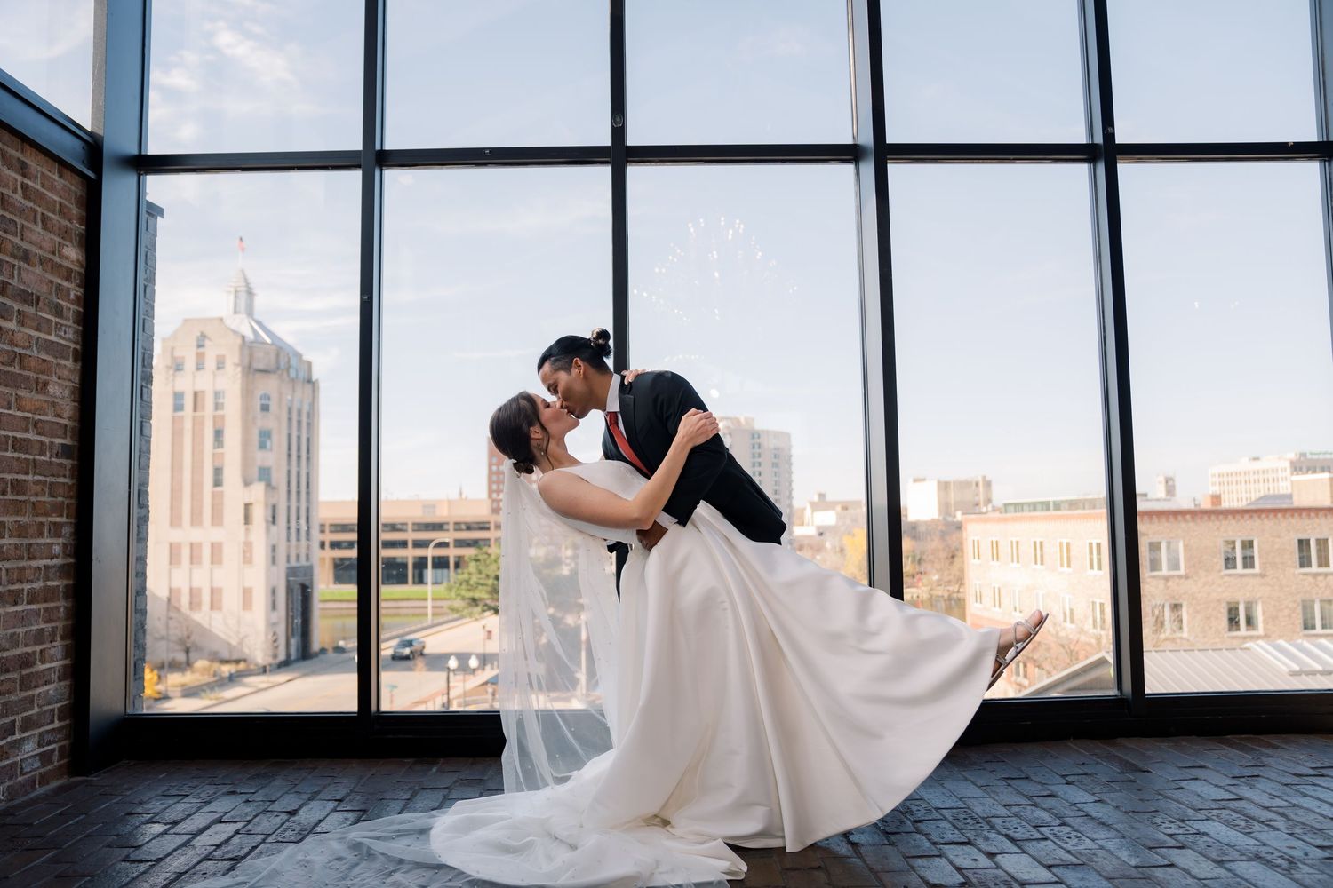 Wedding couple silhouetted against large windows in an urban setting.