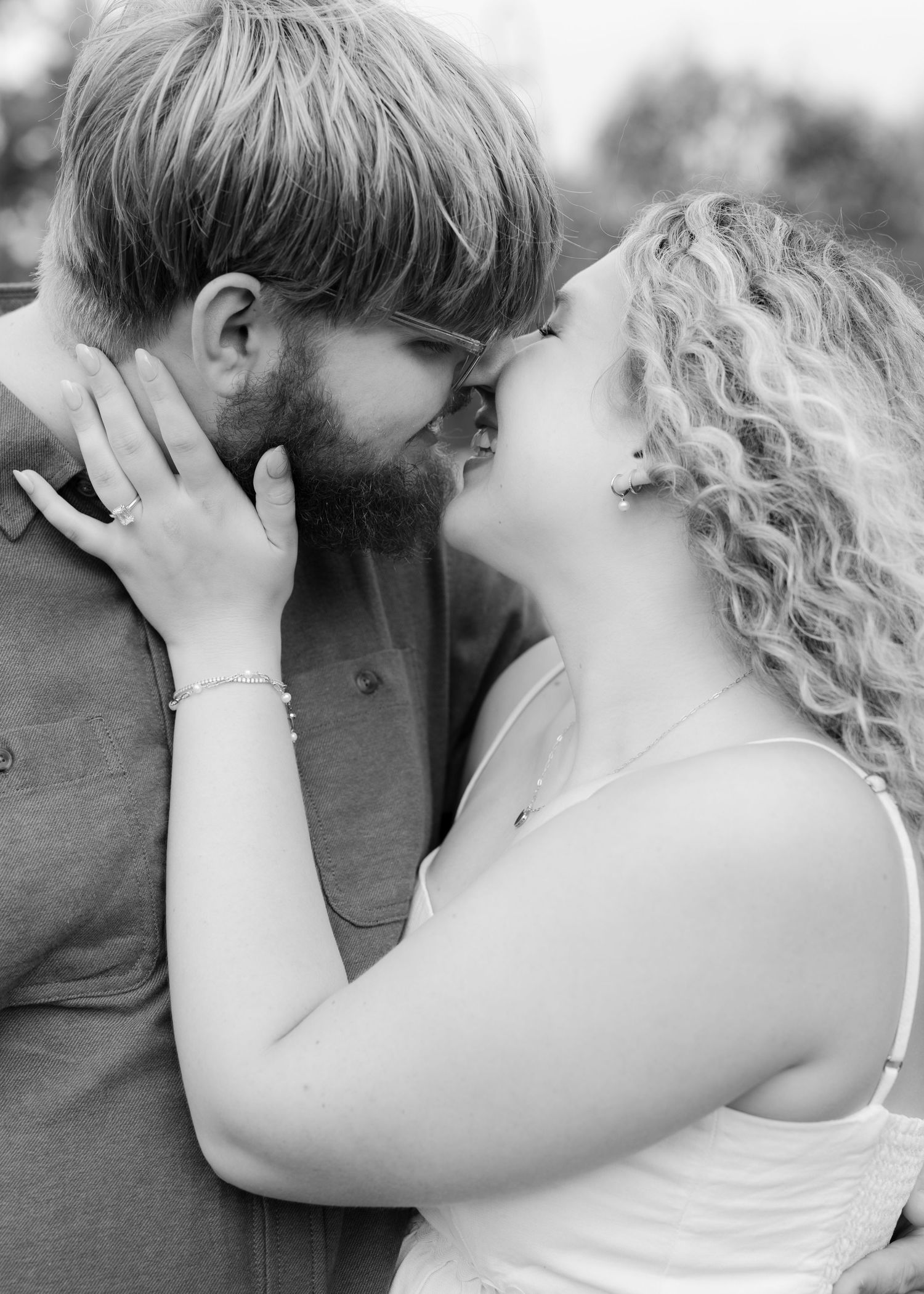 Black and white photo of a couple sharing a romantic kiss, the woman with curly hair wearing a bracelet and ring.