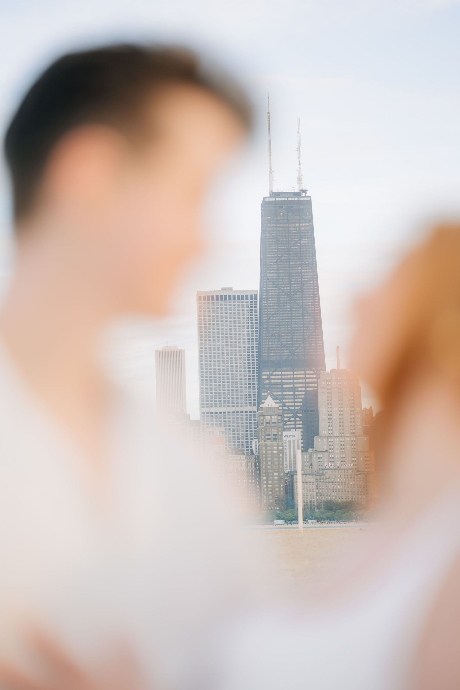 Couple in foreground with Chicago skyline and John Hancock Center visible in soft-focus background.