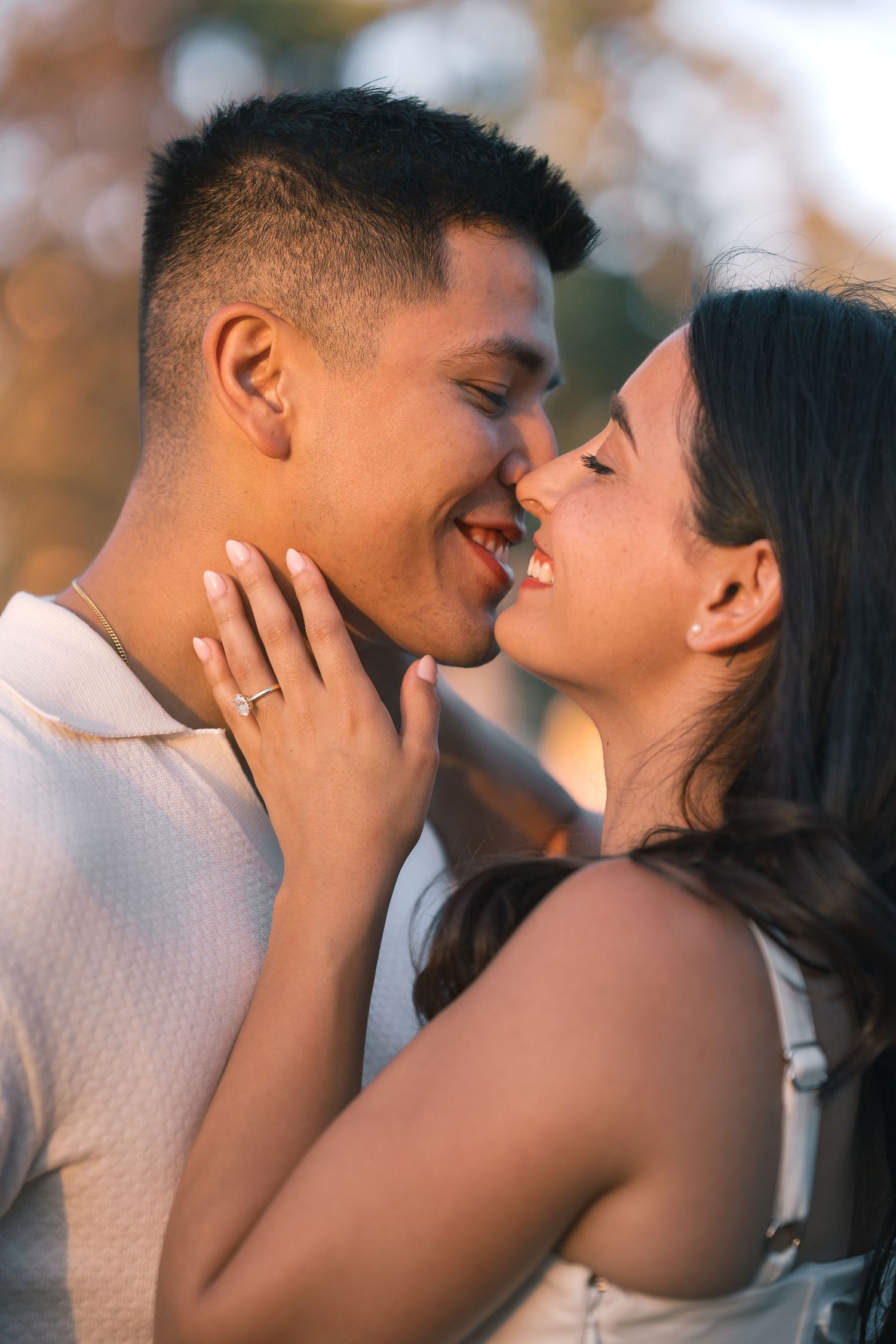 A smiling couple sharing a romantic moment outdoors, with the woman's hand gently resting on the man's chest.