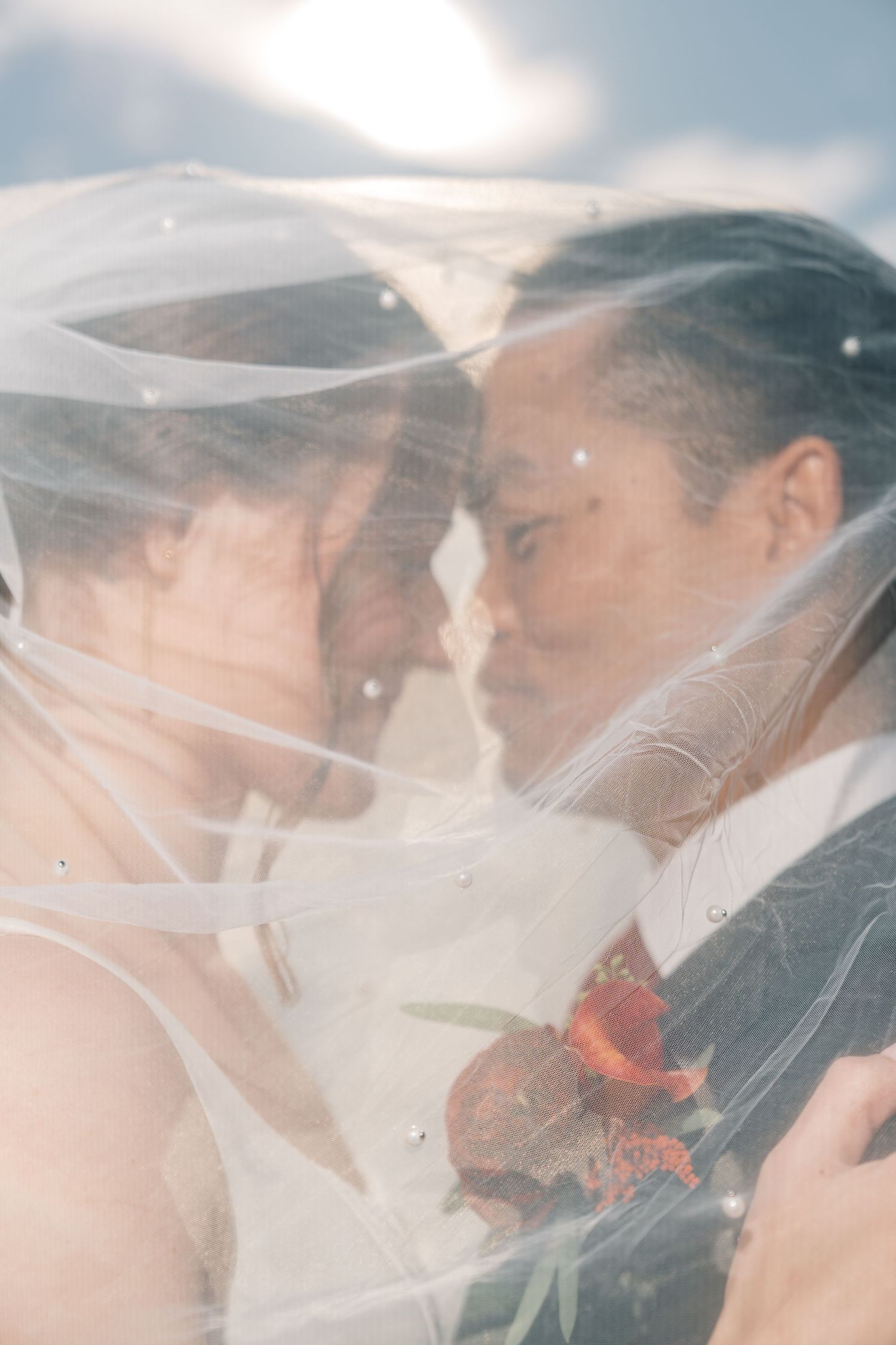 Romantic wedding portrait through flowing veil with soft sunlight.