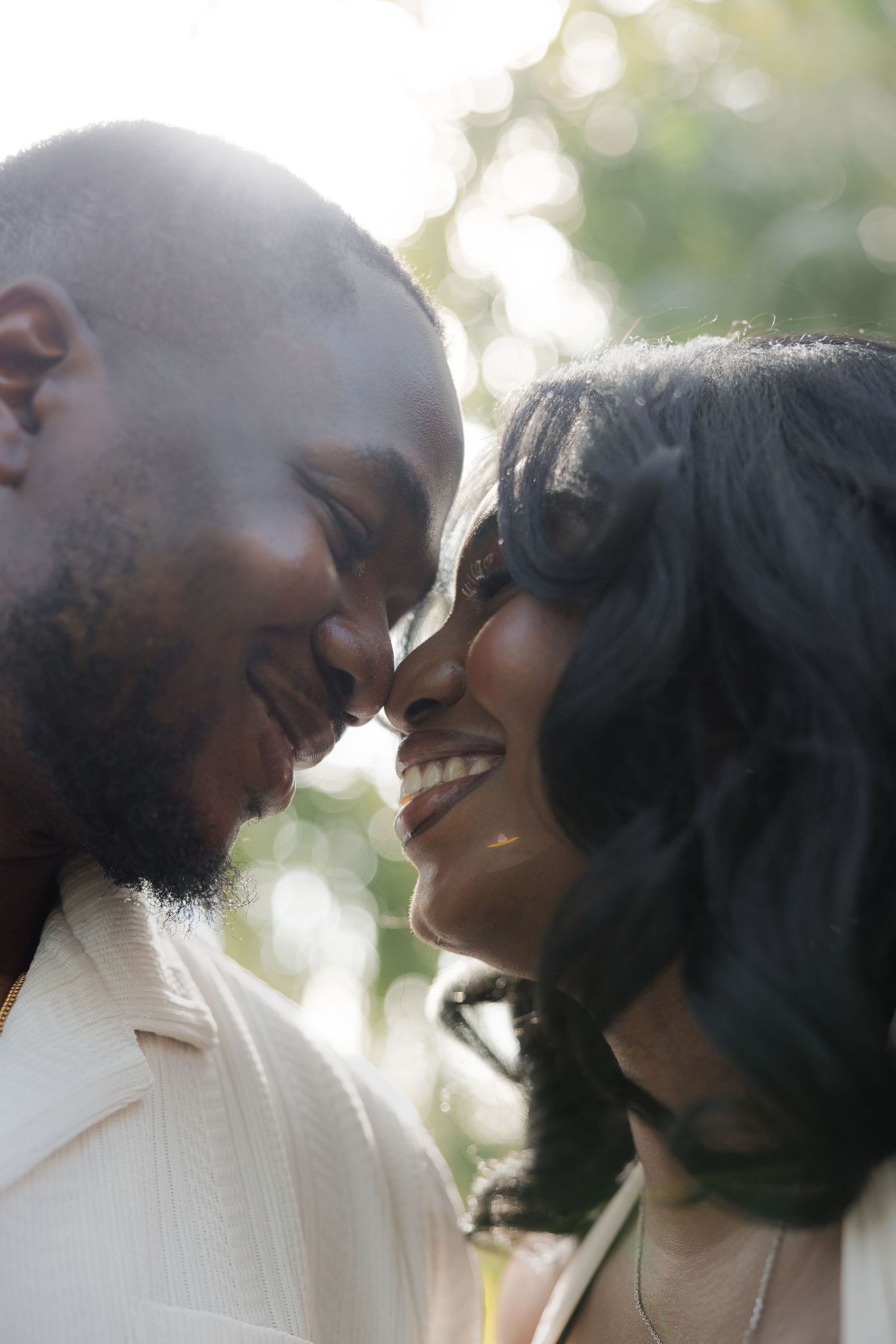 A joyful Black couple smiling and touching foreheads in a tender romantic moment outdoors with soft bokeh lighting.