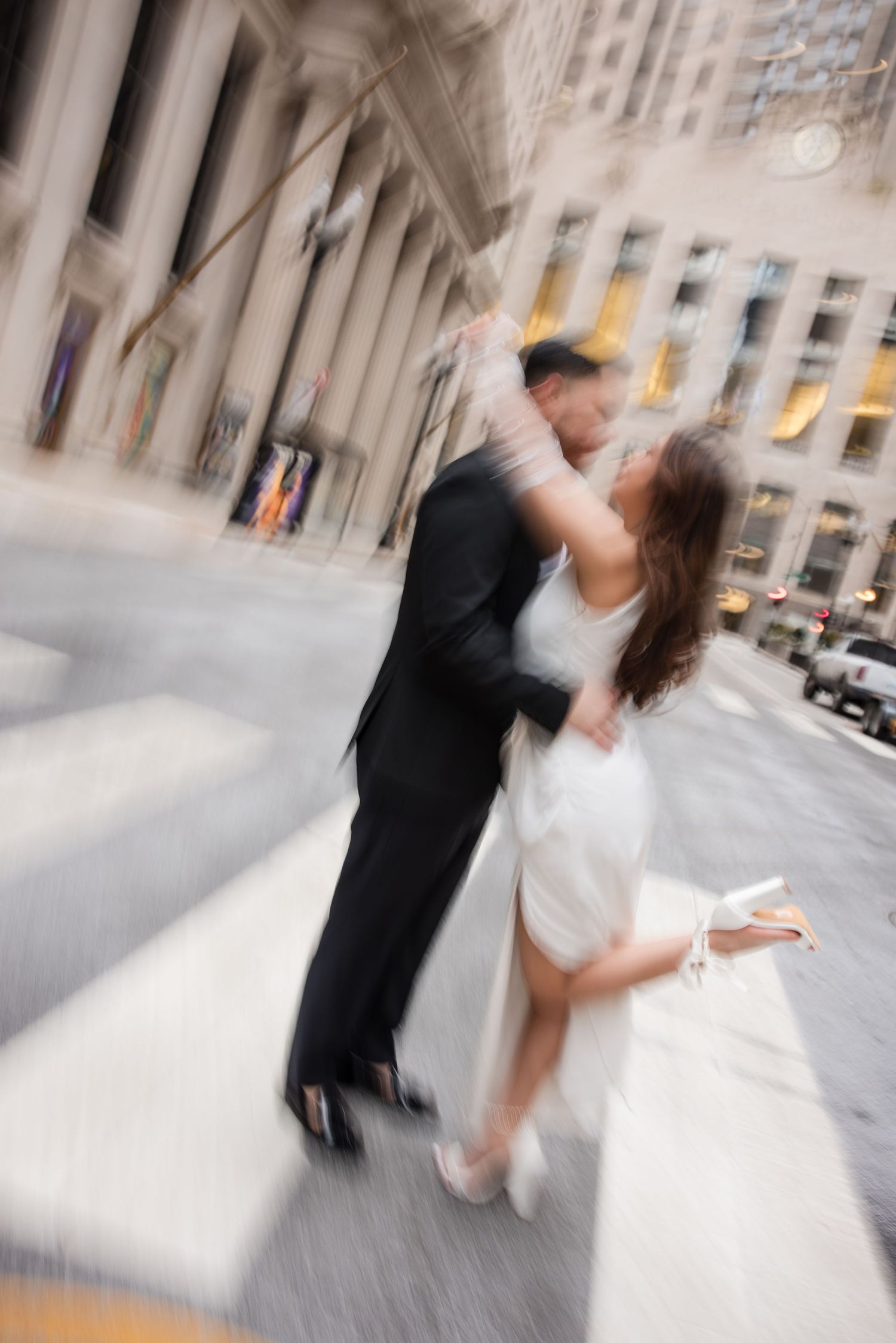 Bride and groom share a romantic kiss on a city crosswalk, captured with motion blur effect.