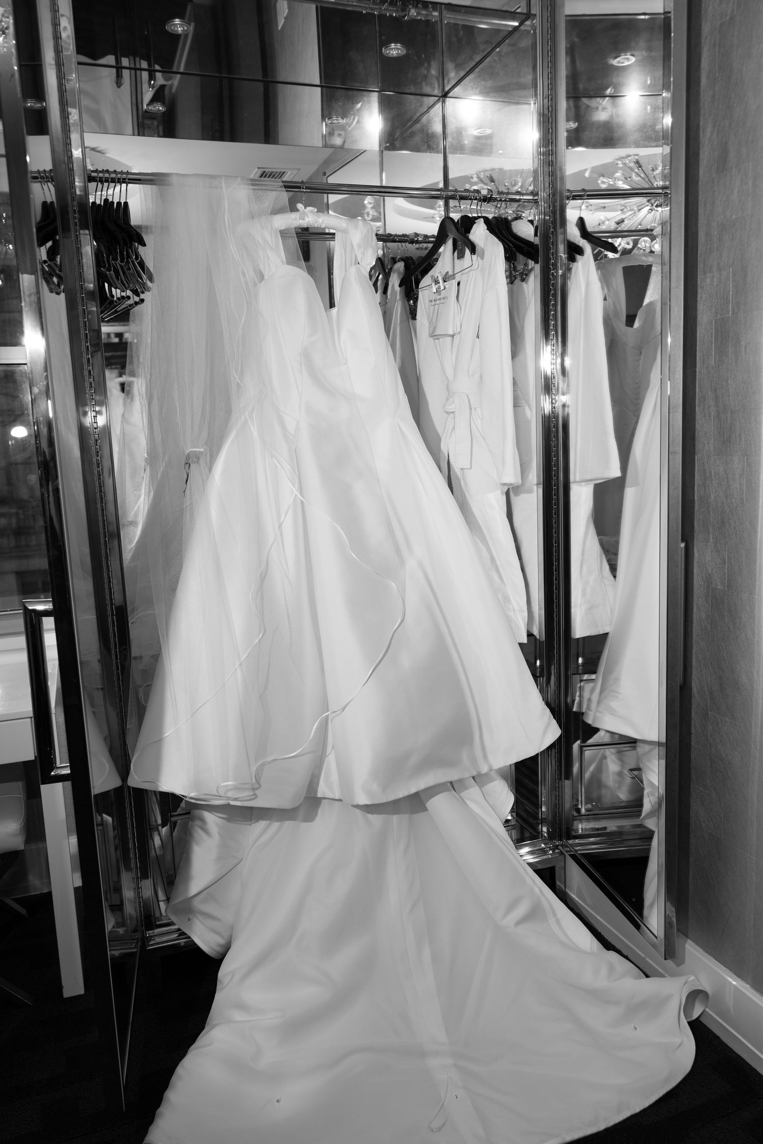 Wedding gowns displayed in a bridal shop with dramatic lighting and mirrors.