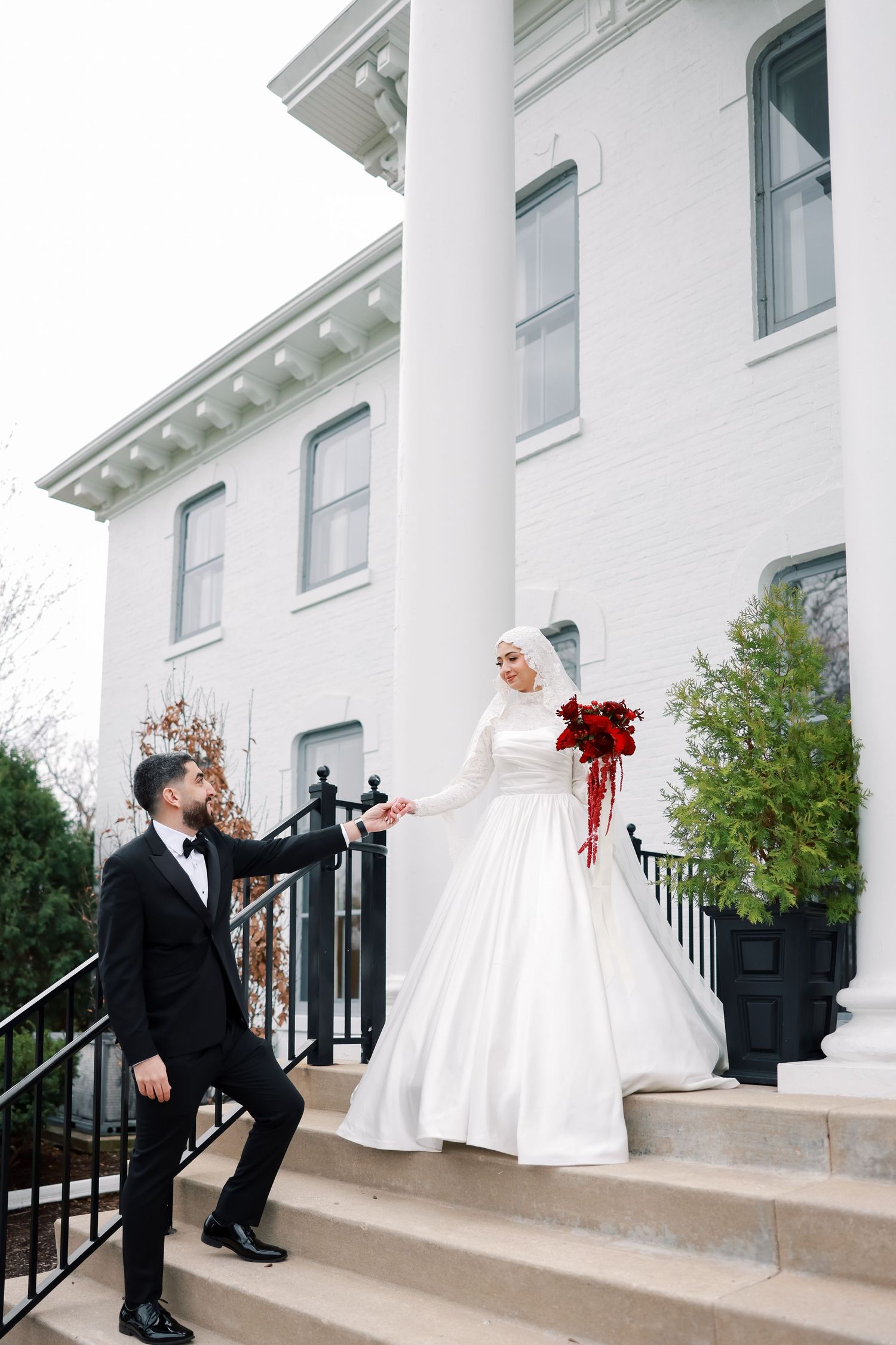 Playful wedding couple poses on steps of white columned building.