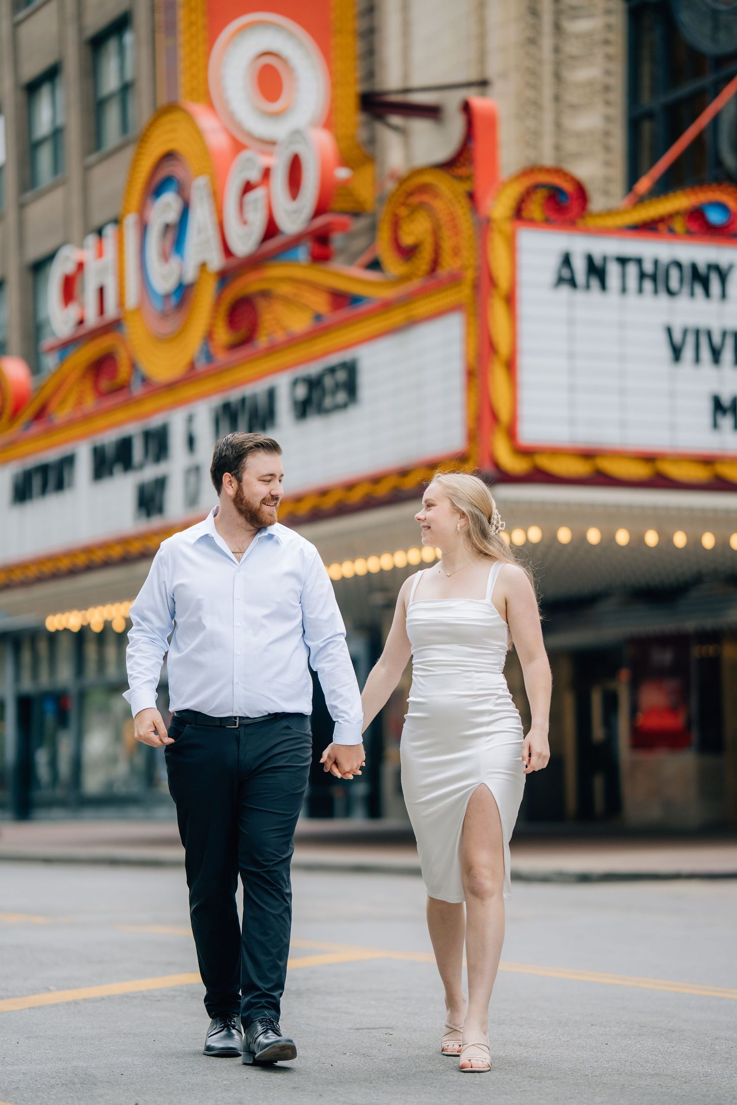 Couple holding hands walking in front of the iconic Chicago Theatre marquee sign on State Street.