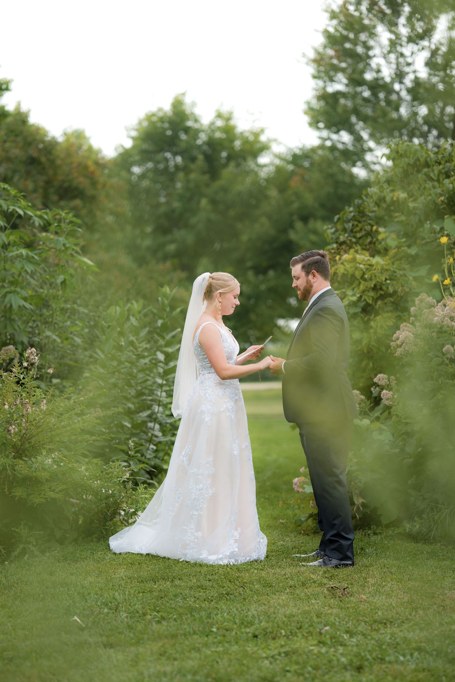Romantic wedding proposal scene captured through greenery in an outdoor garden setting.