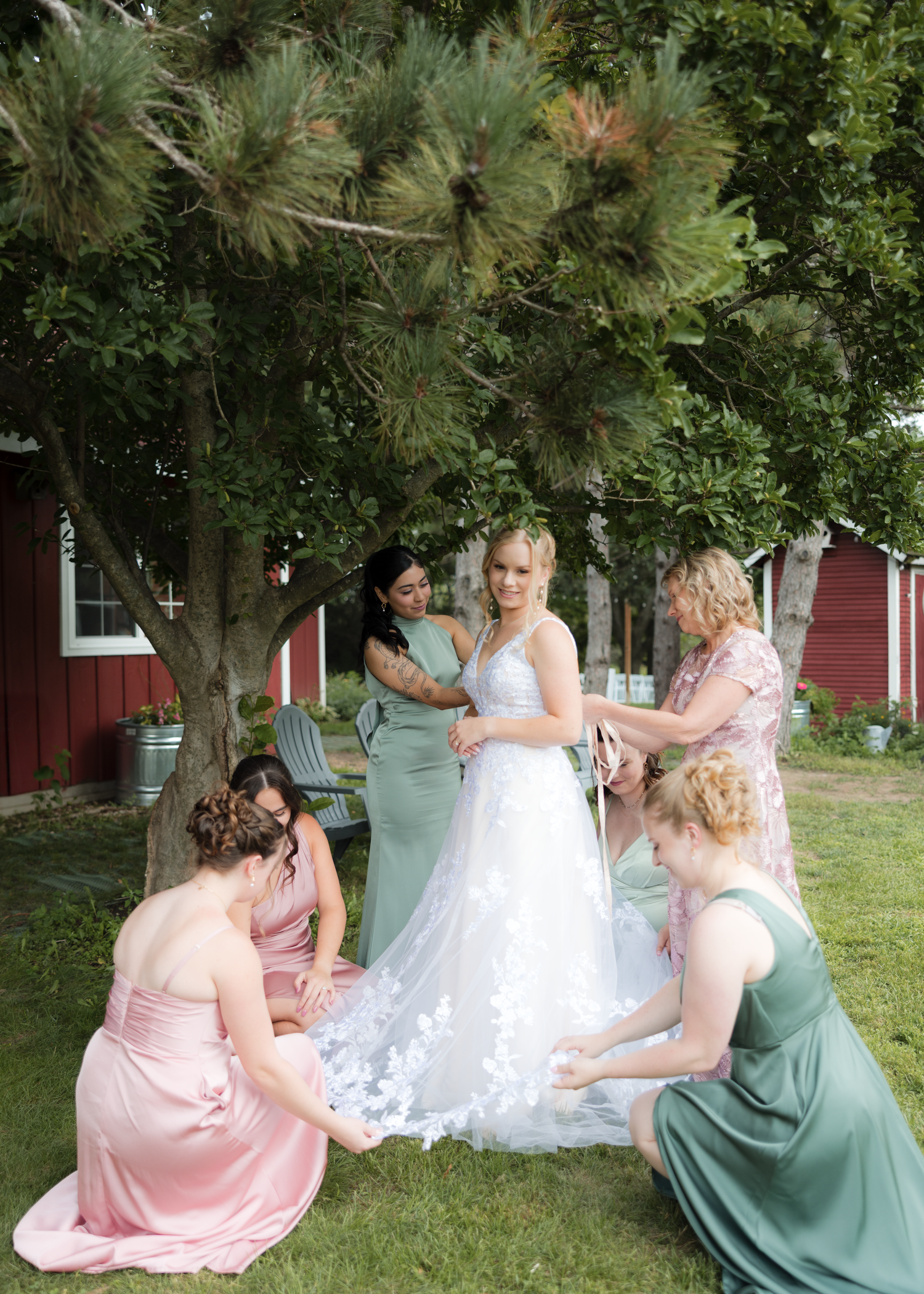 Bridesmaids in pink and mint dresses helping with wedding dress outdoors.