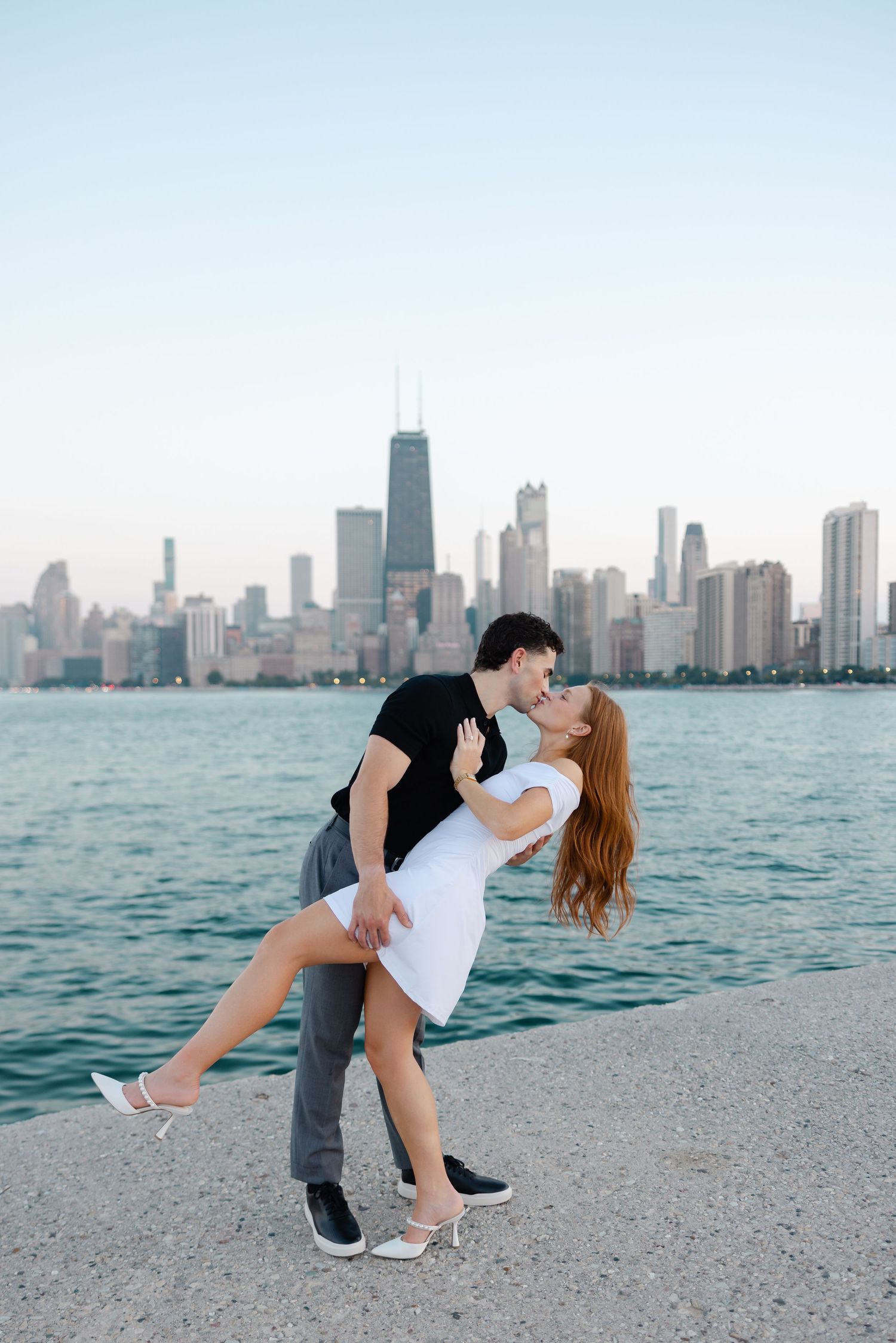 Couple sharing a romantic dip kiss on Chicago lakefront with city skyline backdrop at dusk.