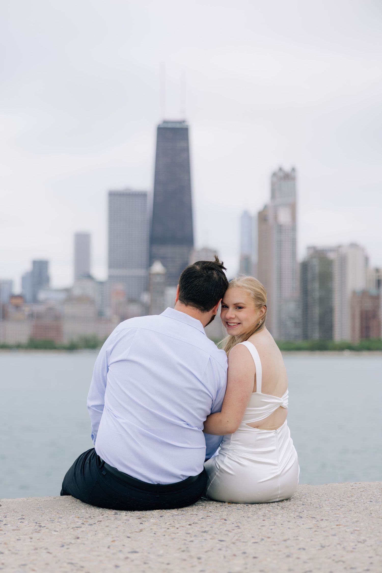 Couple sitting together on Chicago lakefront with city skyline and John Hancock Center in background.