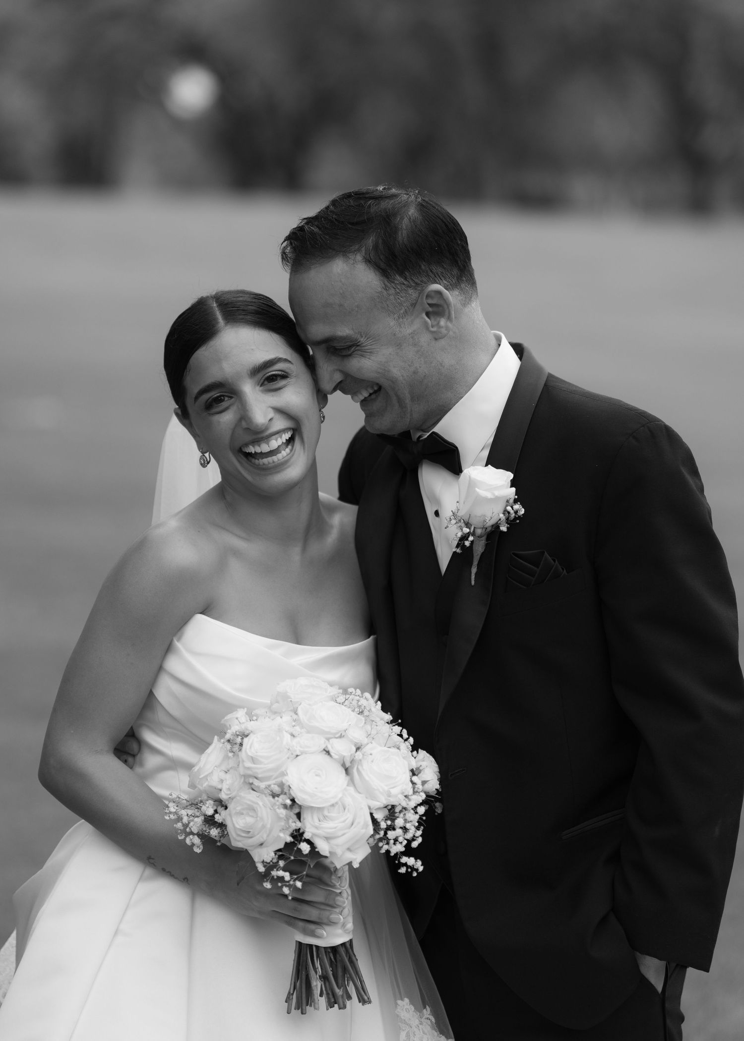 Black and white candid moment of newlyweds sharing laughter outdoors.