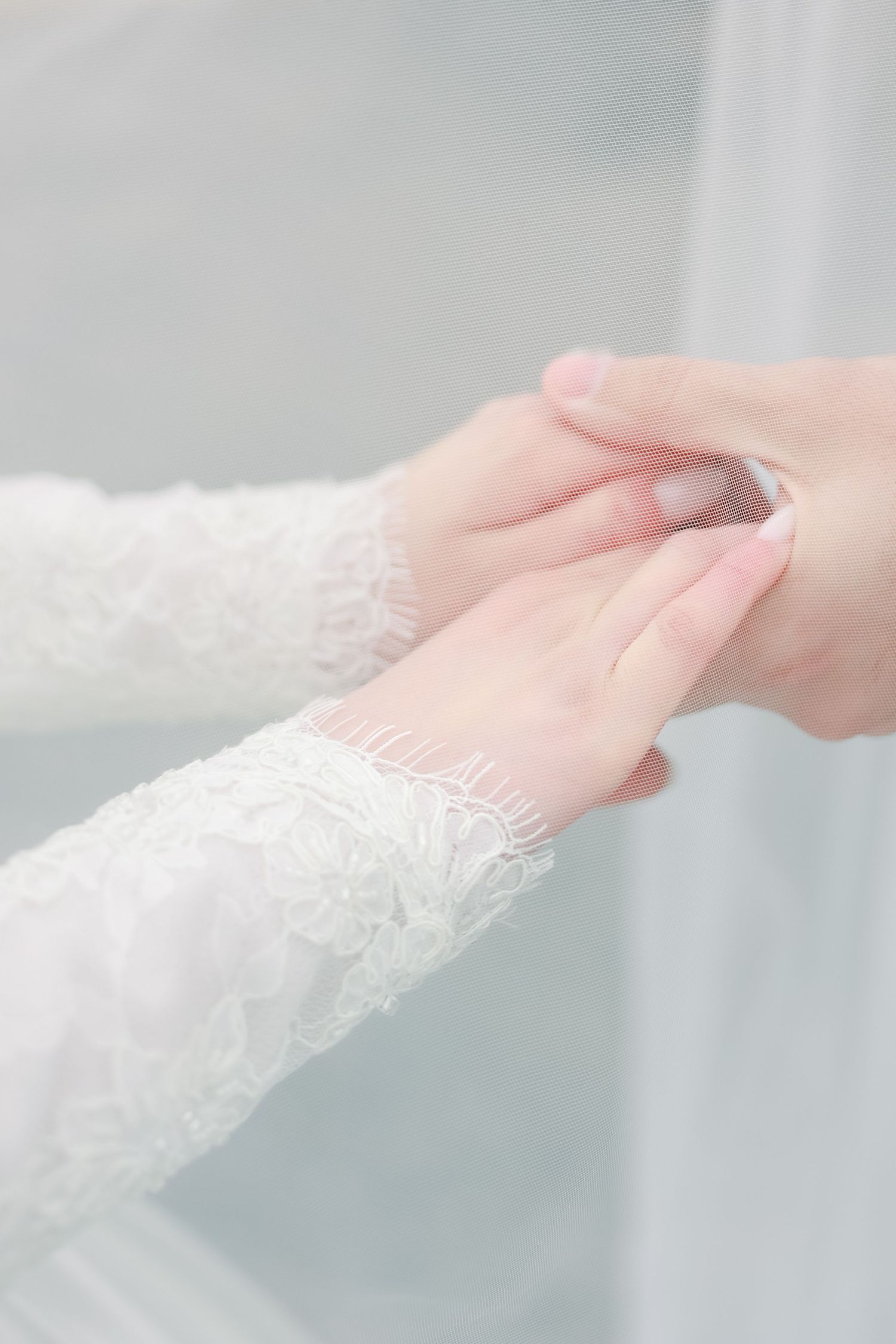 Close-up of delicate lace details on wedding dress sleeve with hands.