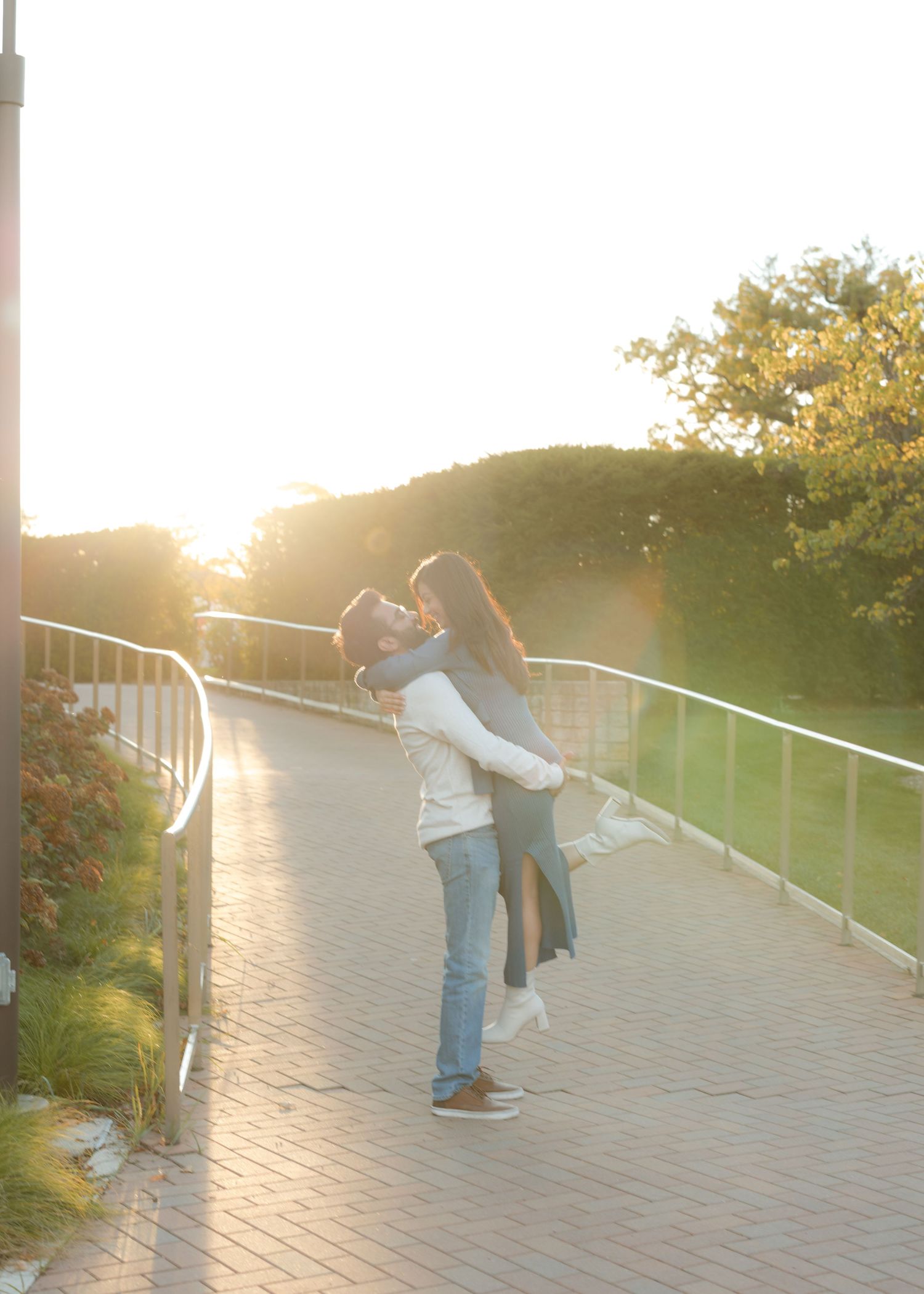 Romantic couple sharing a kiss at sunset on a walkway, man lifting woman in warm golden light.