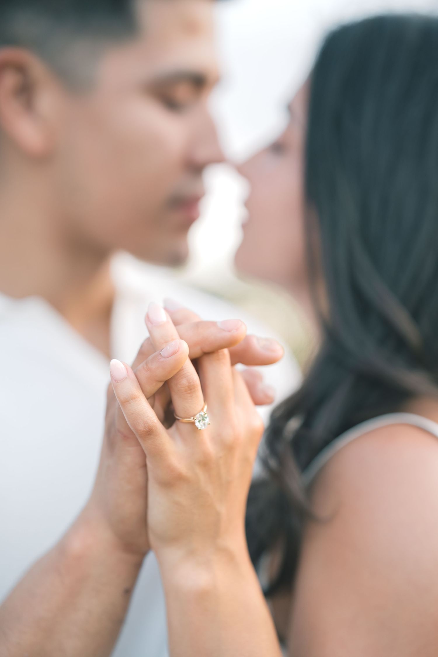 Close-up of couple kissing while showing off an engagement ring on the woman's finger.
