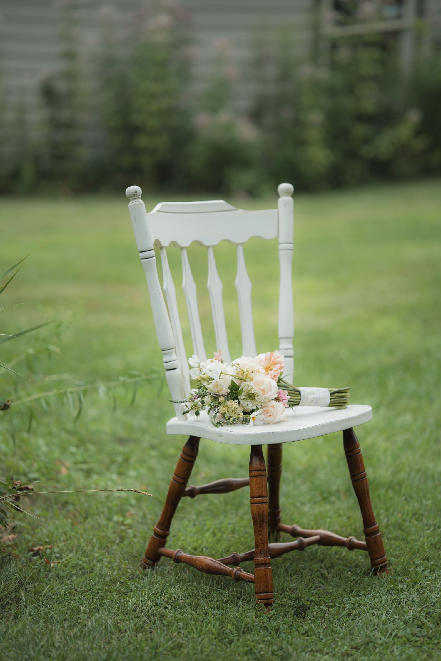 White wooden chair decorated with delicate floral arrangements sits on green grass in a garden setting.