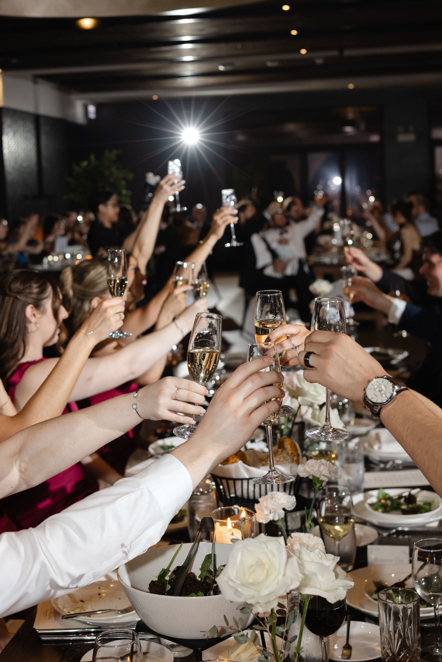 Guests raising champagne glasses in a toast at an elegant wedding reception dinner party.