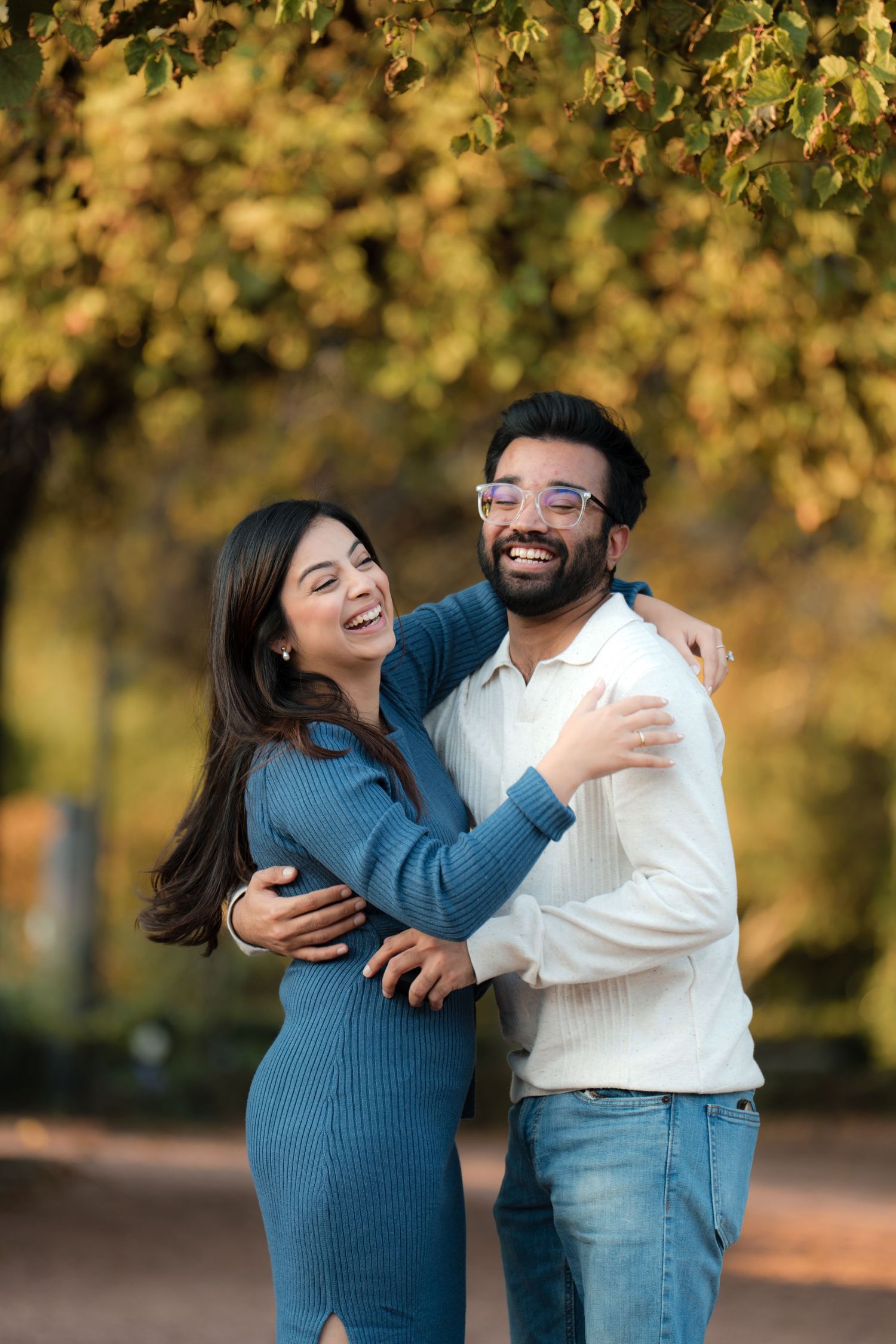 A smiling couple embraces outdoors in a park with vibrant autumn yellow foliage in the background.