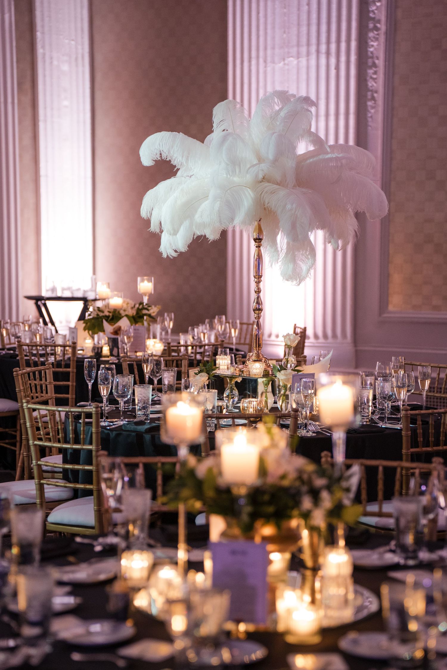 Elegant wedding reception tables with white feather centerpieces and glowing candles.