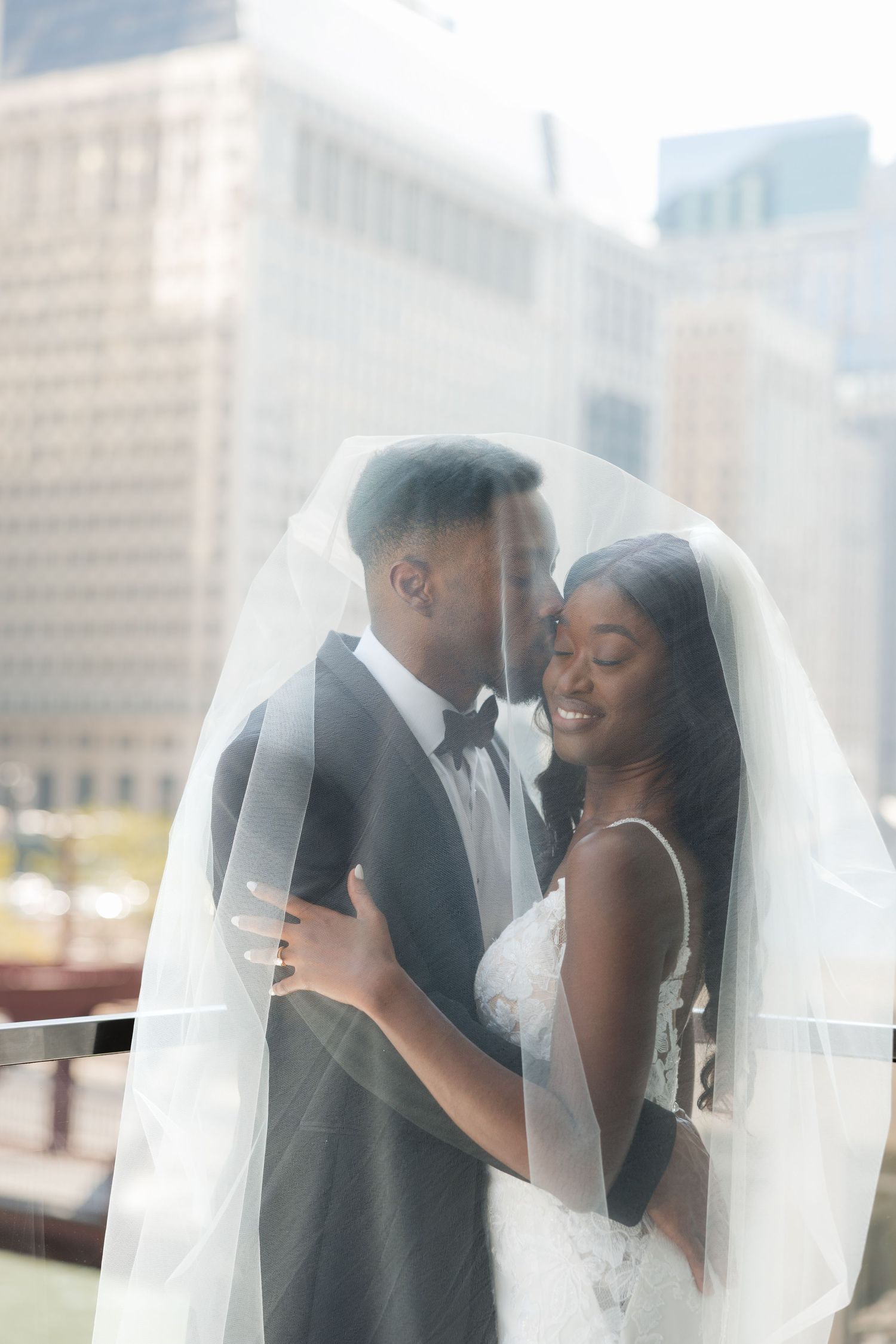 Romantic wedding couple shares intimate moments under flowing veil with city skyline backdrop.