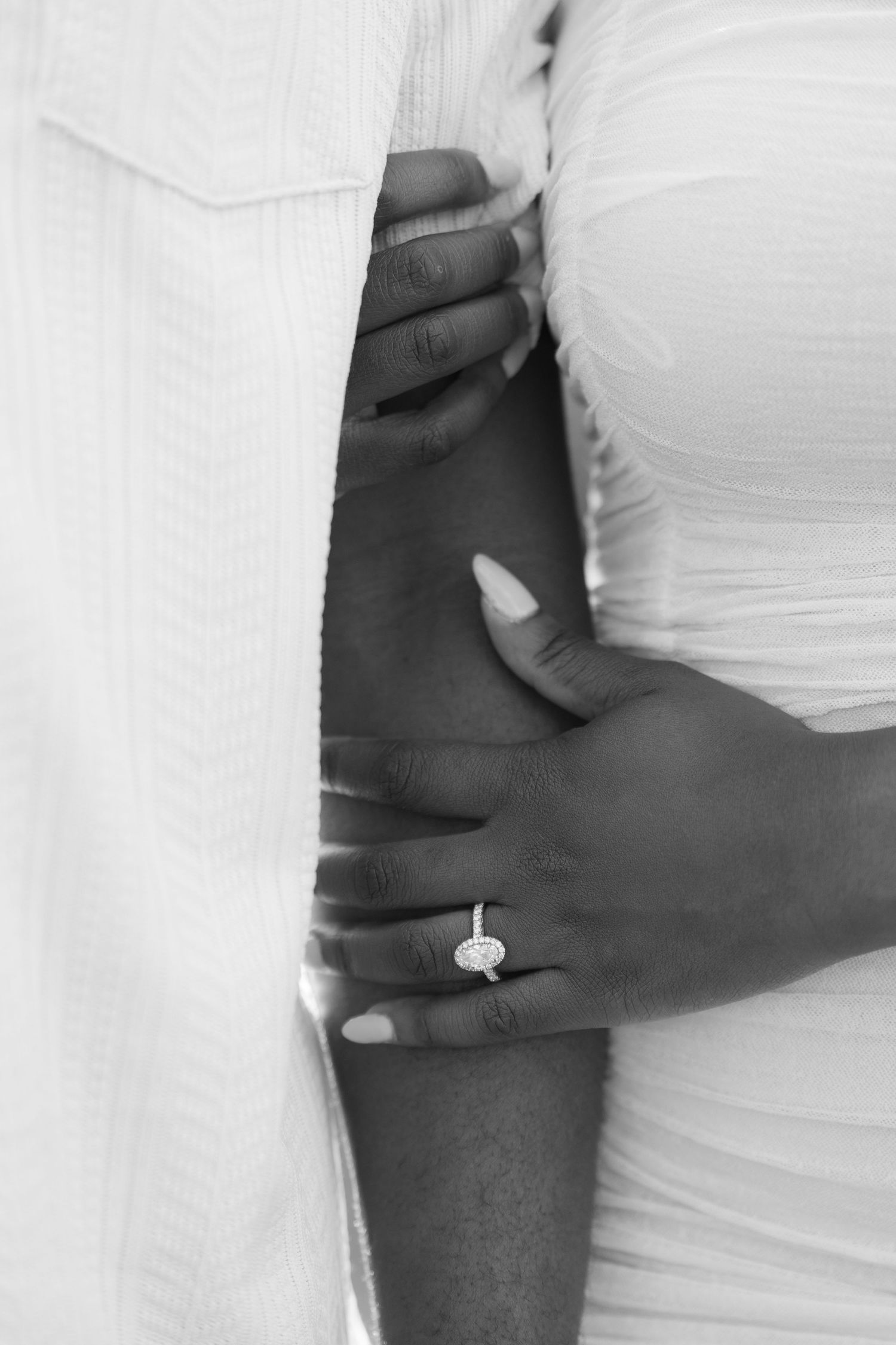 Black and white photo of a couple embracing, woman wearing an oval diamond engagement ring on her finger.