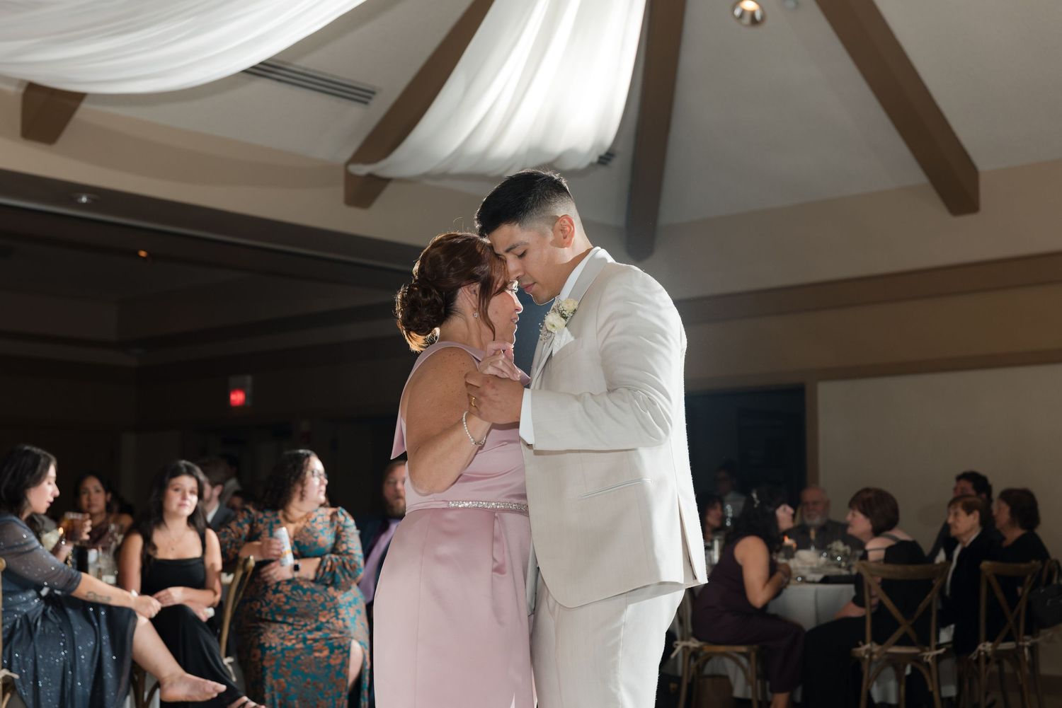 Wedding couple shares their first dance in reception hall with guests looking on.