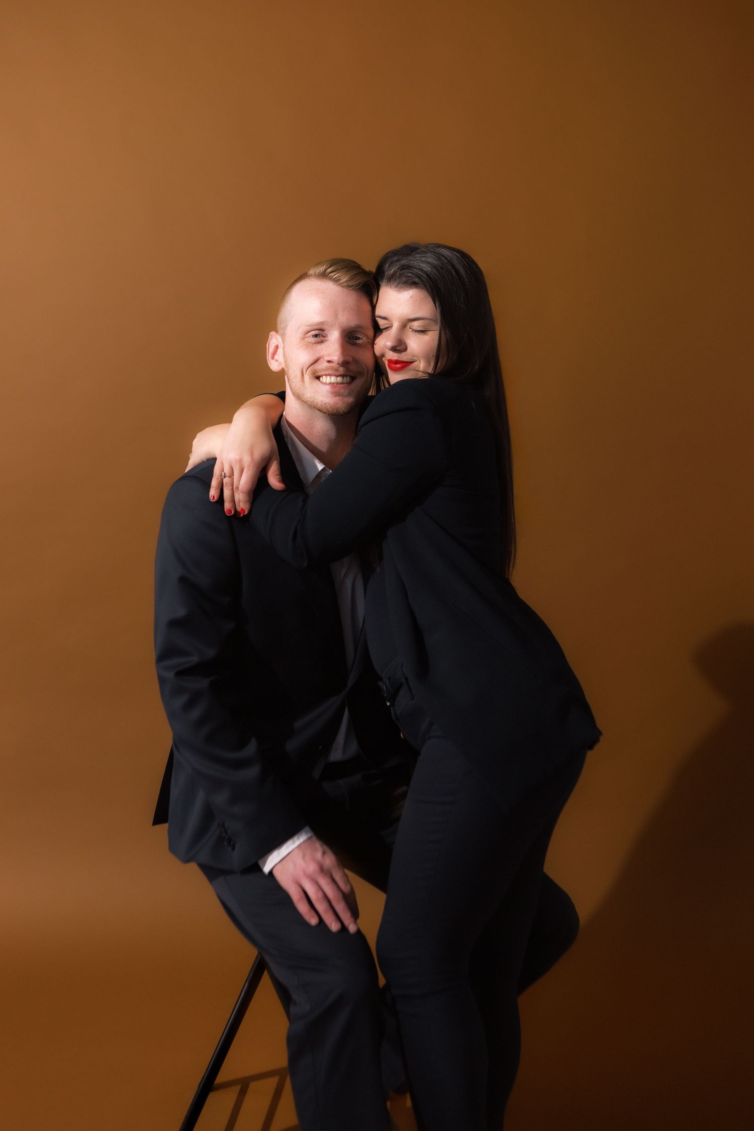 Playful couple in formal black attire laughing during a photo shoot.