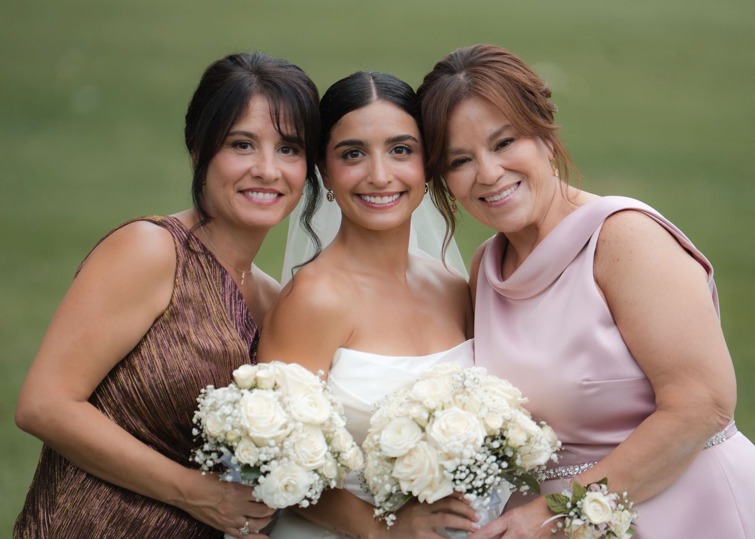 Bridesmaids in pink dresses pose together with white bouquets on a grassy lawn.