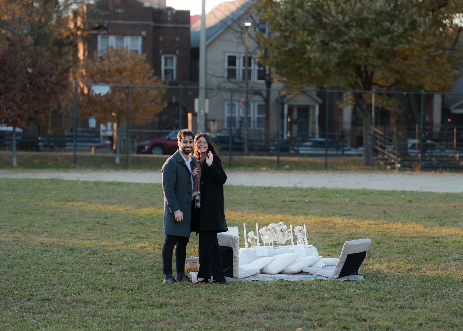 Couple posing together in a park with a white sofa and candles setup for a romantic outdoor proposal.