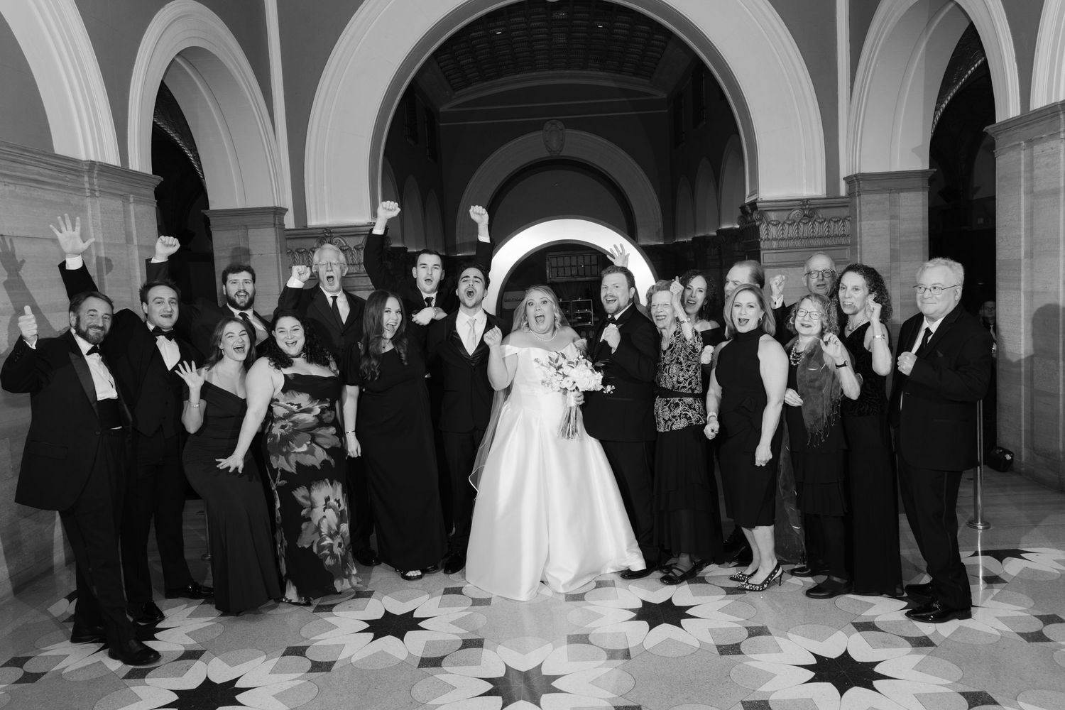 Large wedding party gathering in an elegant arched hallway for formal photos.