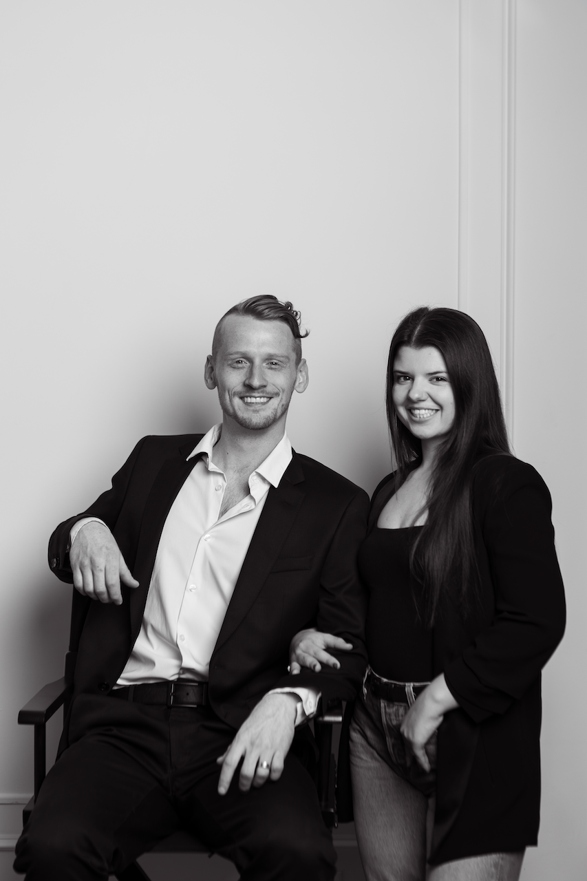 Couple in black and white outfits laughing during studio photoshoot.