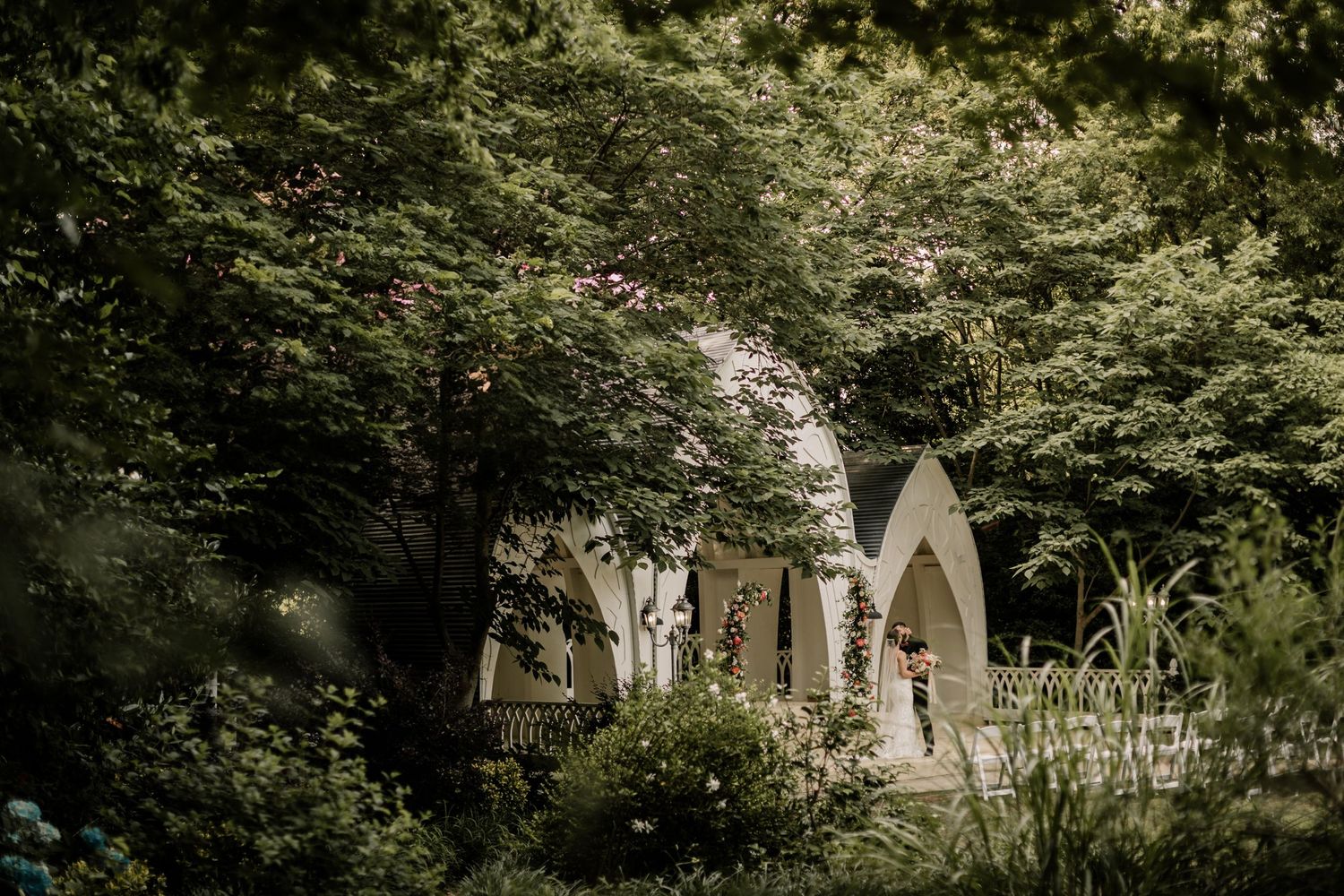 A white chapel nestled among lush green trees creates a serene wedding venue setting.
