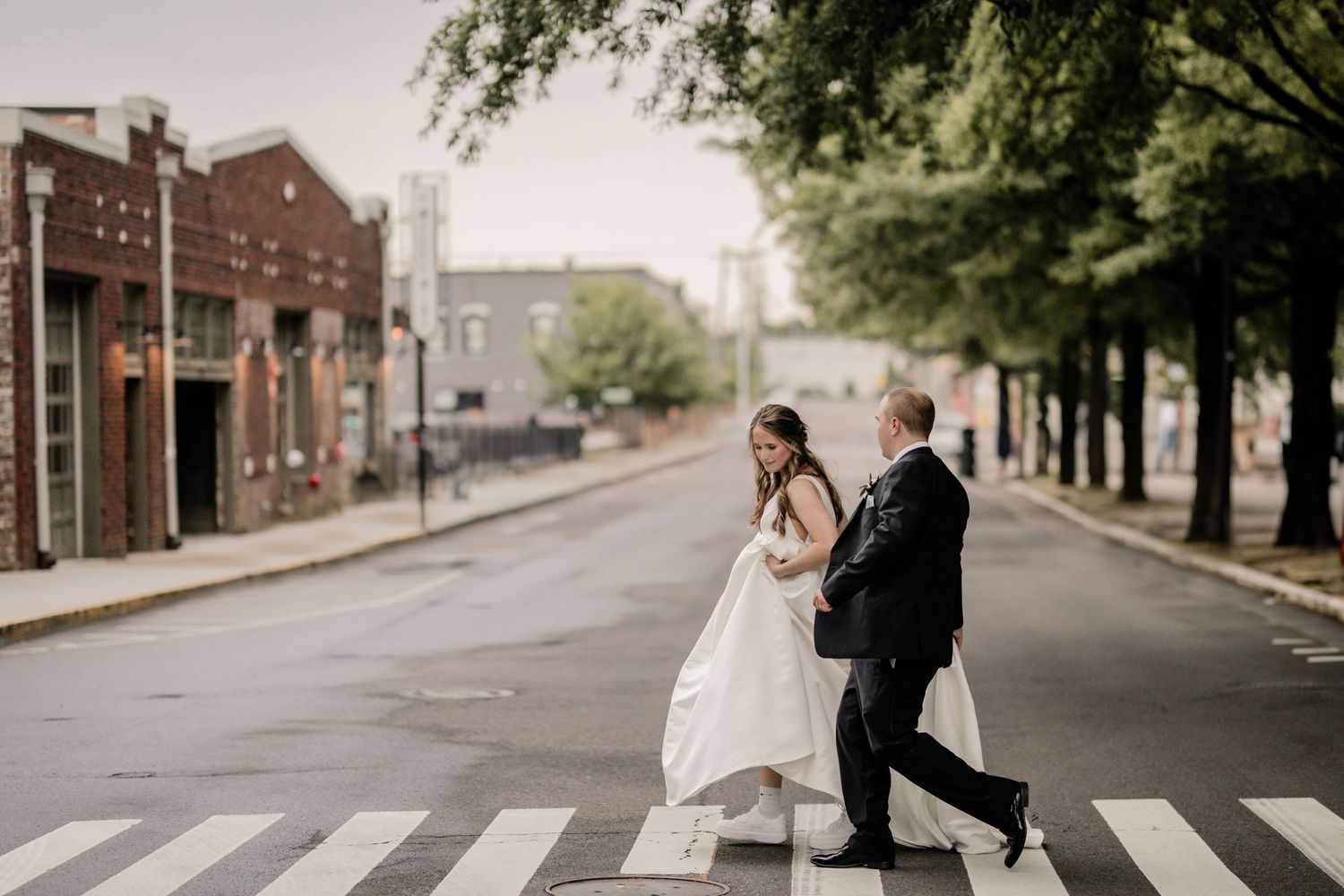 Newlyweds playfully cross urban street together during wedding photoshoot.