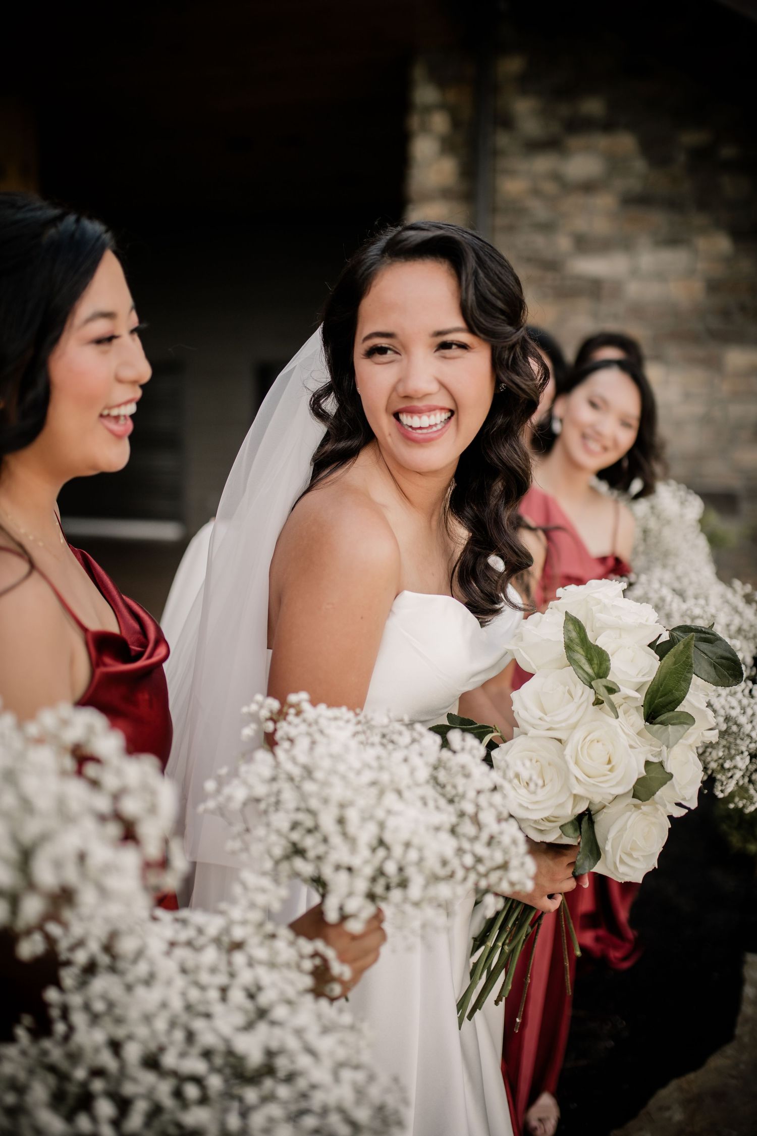 Bridal party with white roses and baby's breath bouquets share joyful moment together.