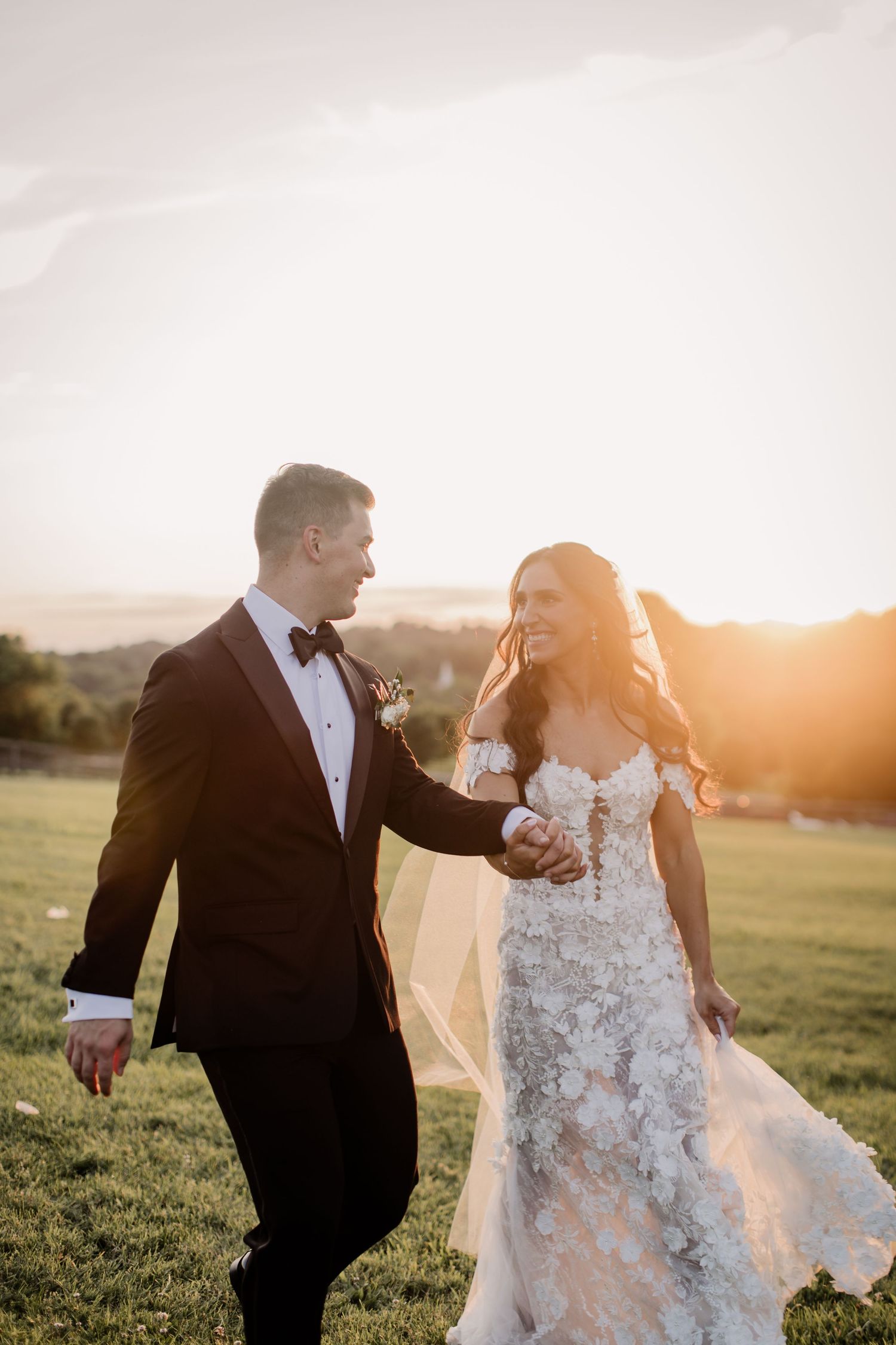 Newlyweds share intimate moment in golden sunset light on grassy hillside.