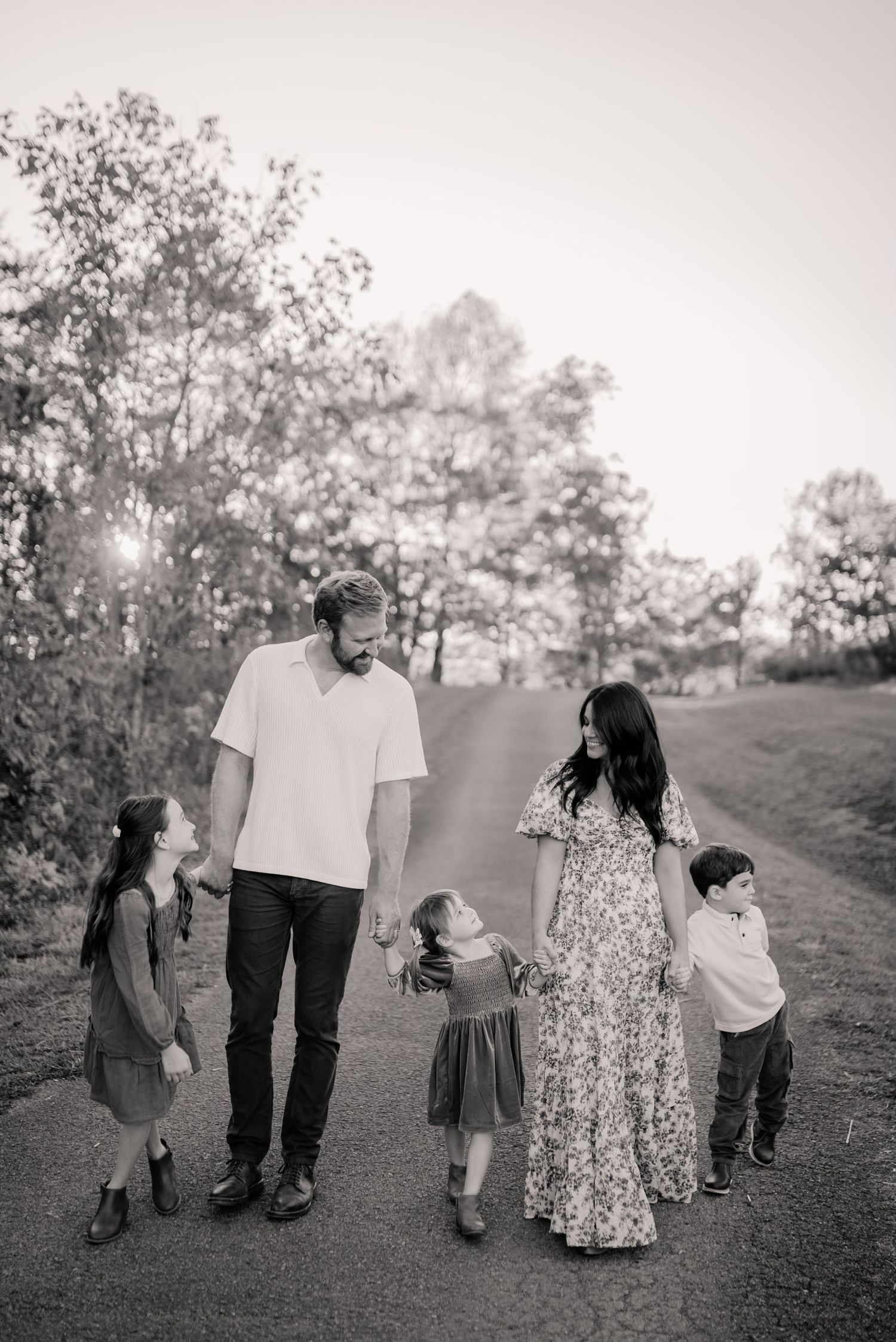 A family walks together along a hillside path in black and white, creating a series of candid silhouettes against nature.