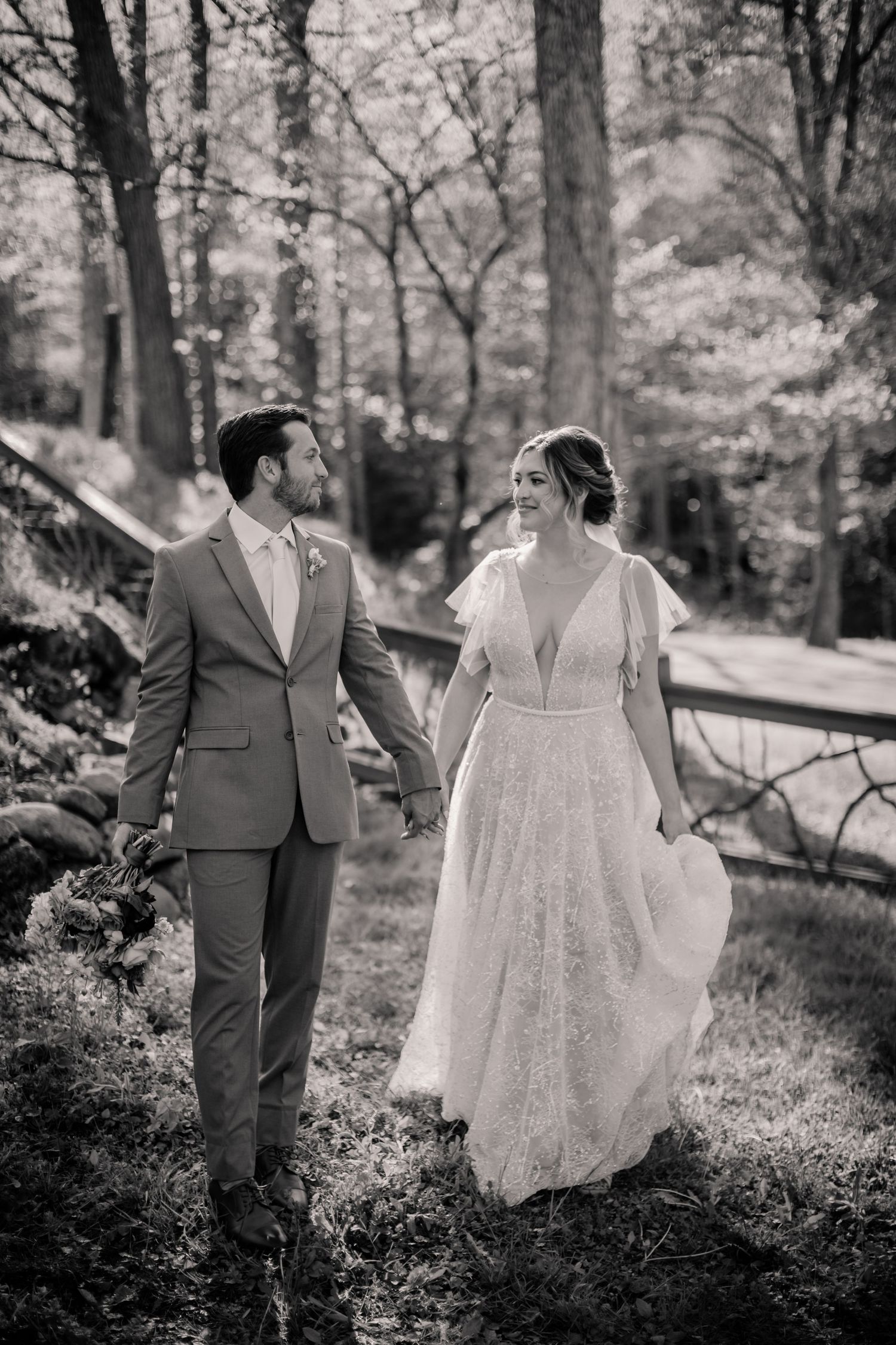 A romantic black and white photo of newlyweds walking together in a wooded forest setting.